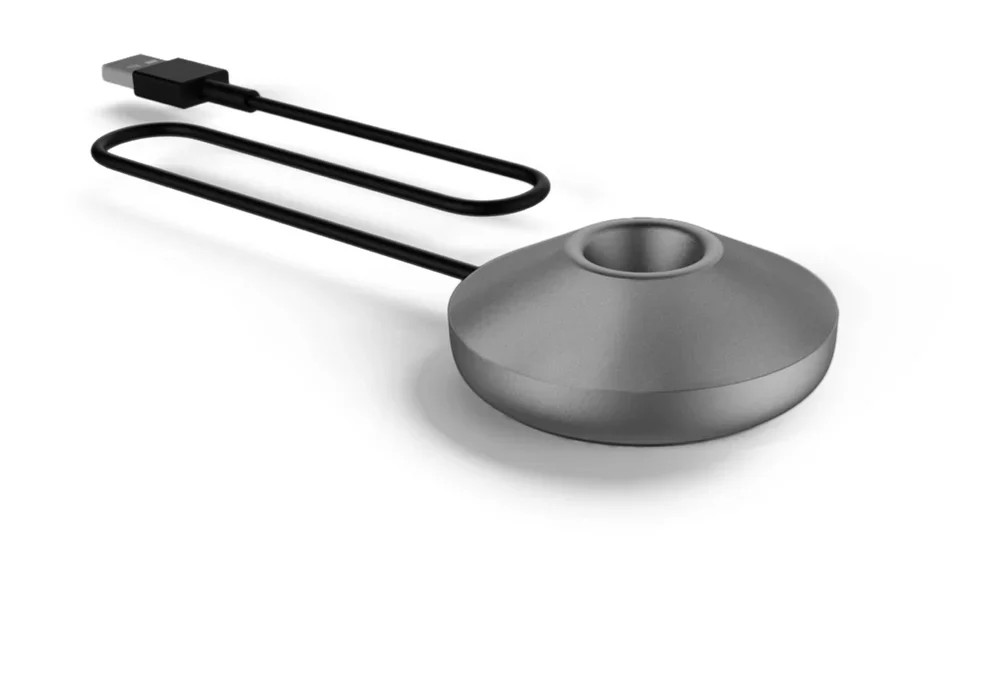 Egy szürke, kerekített töltődokkoló középső mélyedéssel és egy csatlakoztatott fekete USB-kábellel.