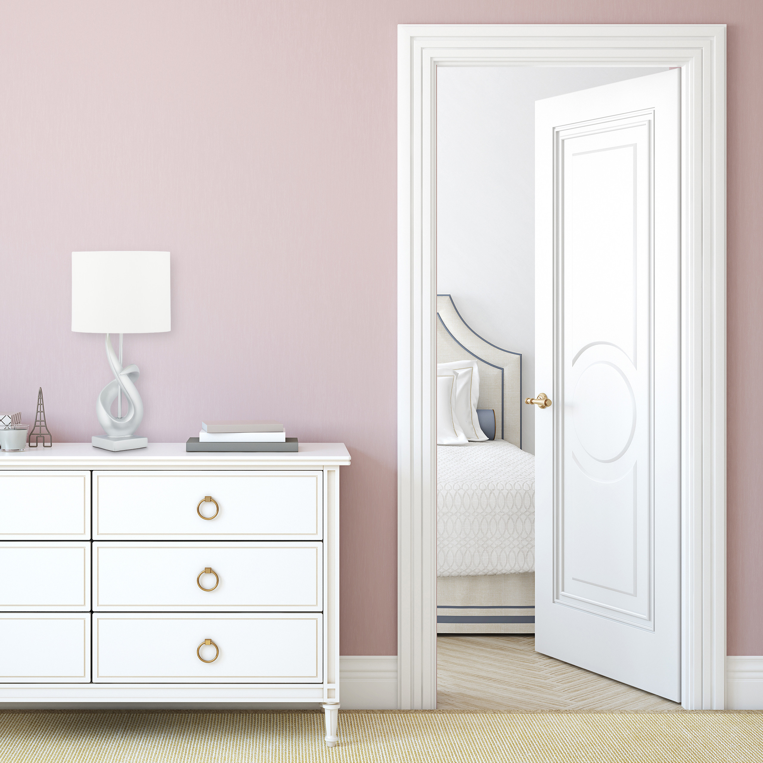 Eine weiße Kommode mit Lampe steht an einer rosa Wand neben einer offenen weißen Tür, die den Blick auf ein Bett freigibt.