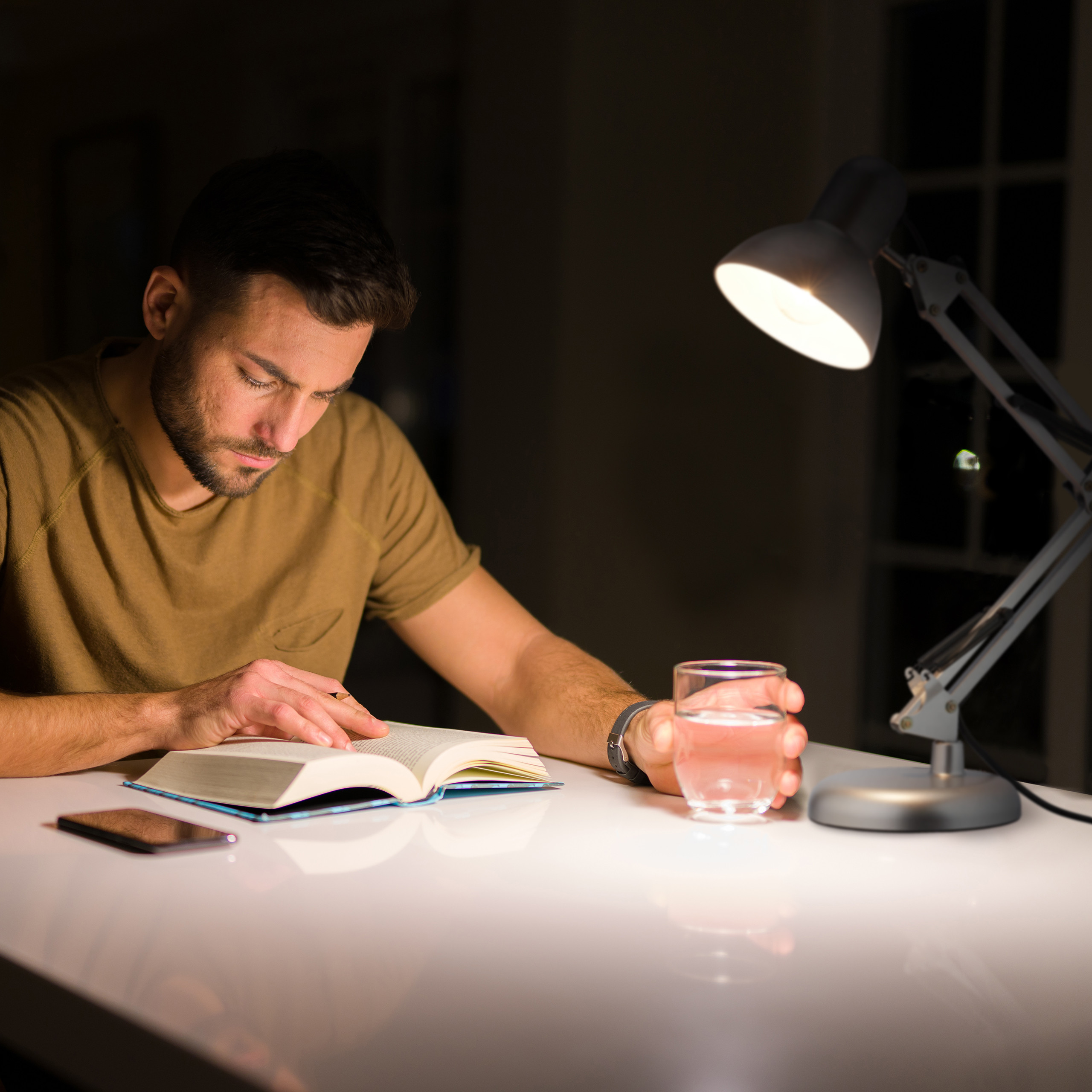 Ein Mann liest nachts an einem Tisch, beleuchtet von einer Lampe.