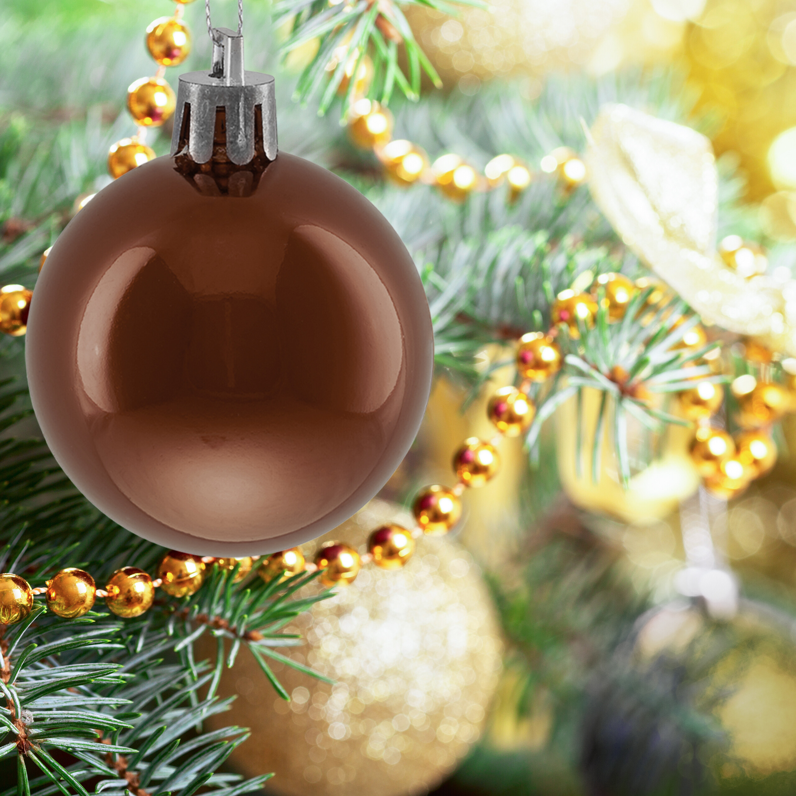 Eine glänzende braune Weihnachtskugel hängt an einem grünen Tannenbaum mit goldenen Perlenketten.