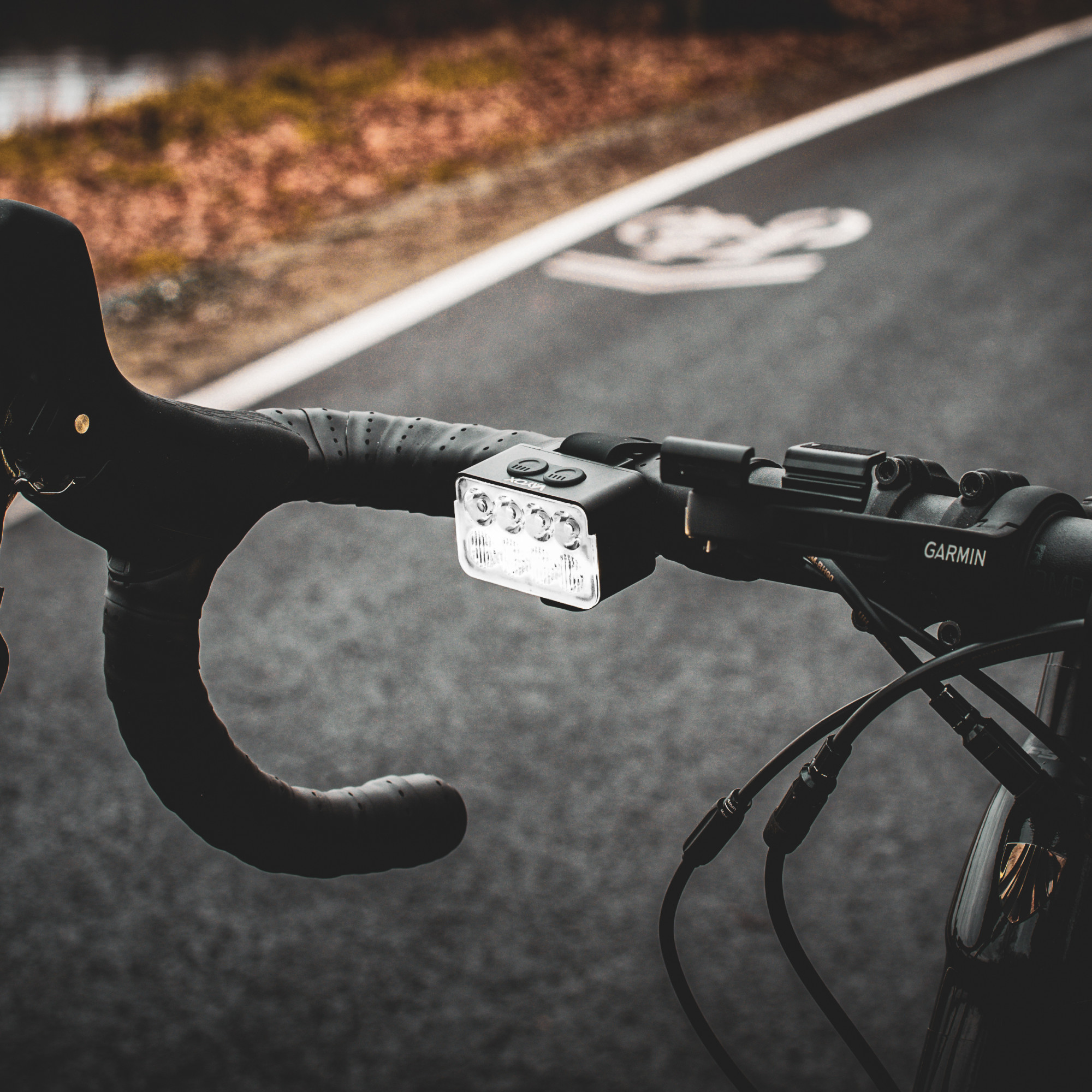 Kierownica roweru z jasną lampką LED na asfaltowej ścieżce rowerowej z oznakowaniem.
