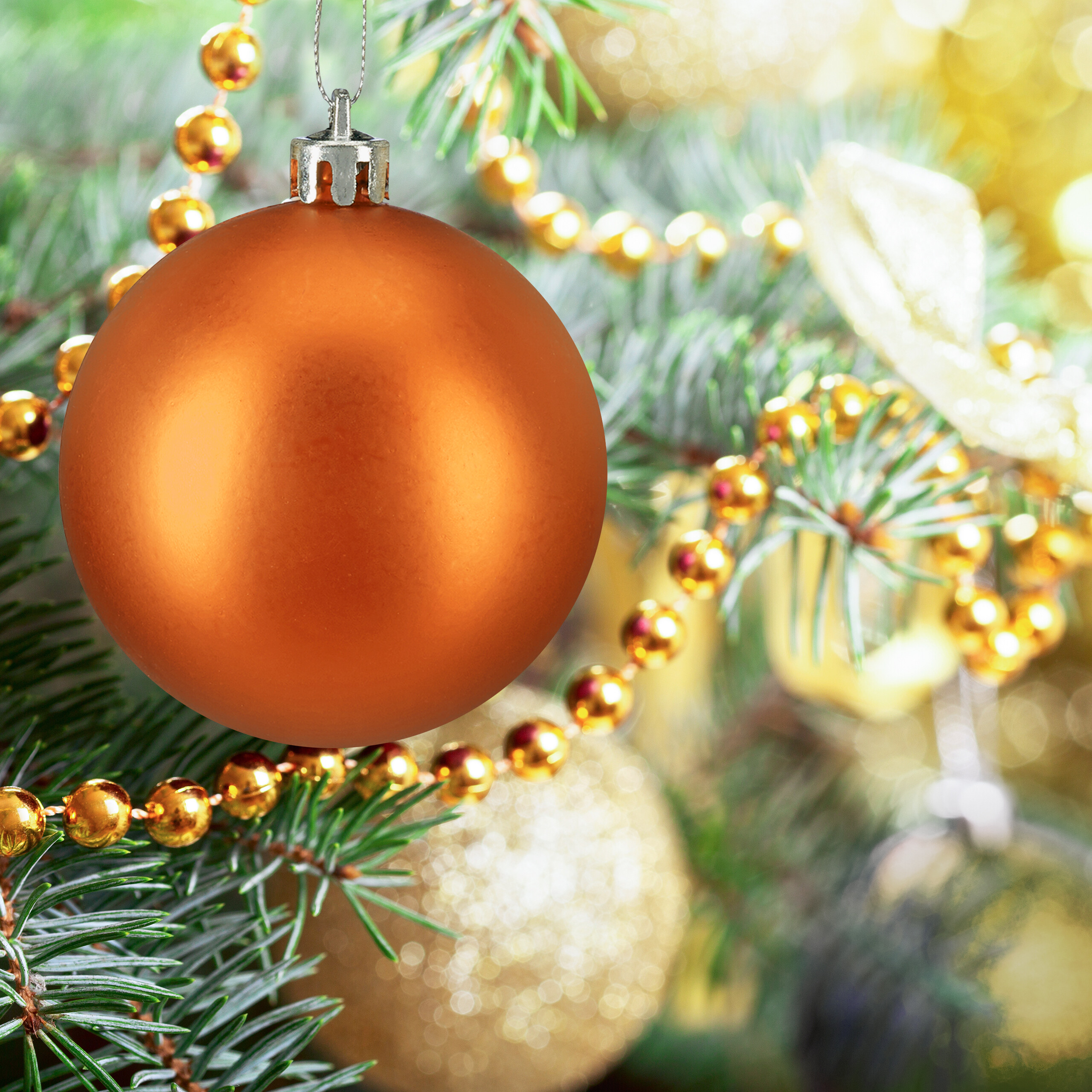 Eine glänzende orangefarbene Weihnachtskugel hängt an einem grünen Weihnachtsbaum mit goldenen Perlen.