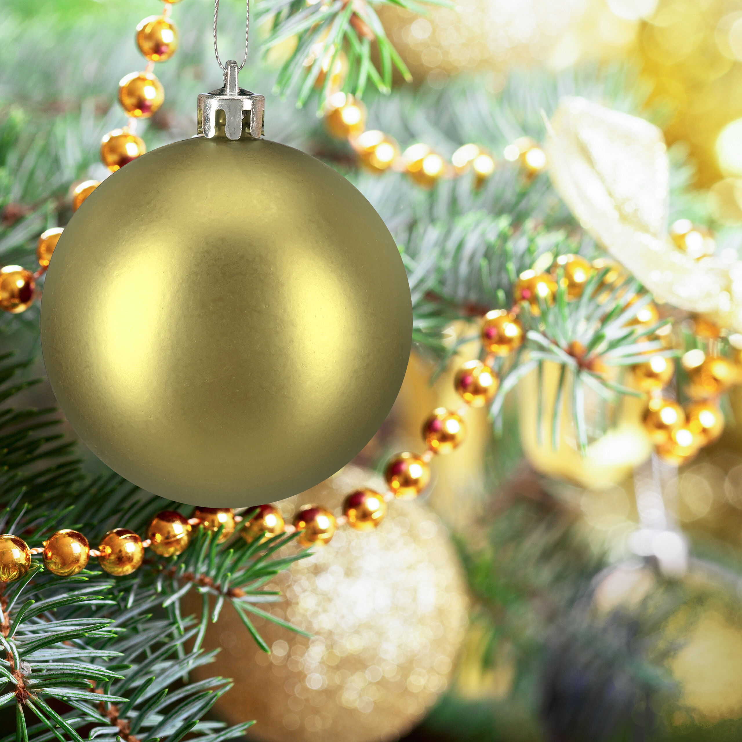 Eine matte goldene Weihnachtskugel hängt an einem Weihnachtsbaum, umgeben von Tannengrün und goldenen Perlenketten.