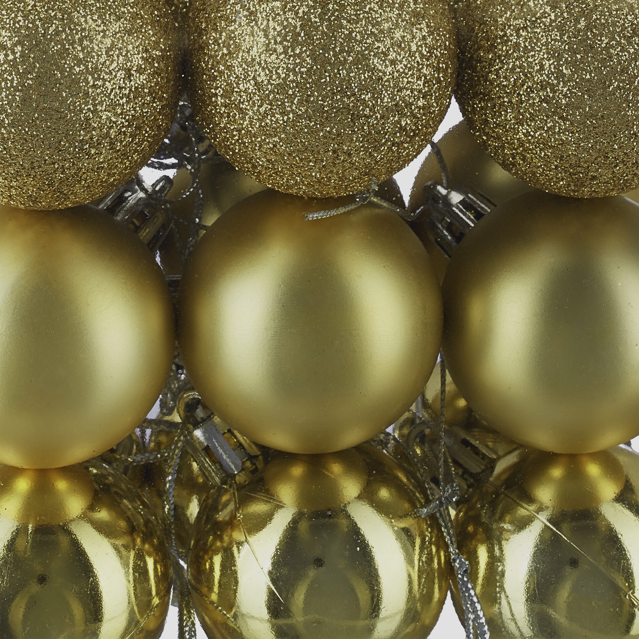 Eine Nahaufnahme von glänzenden, matten und glitzernden goldenen Weihnachtskugeln, gestapelt mit silbernen Hängern.