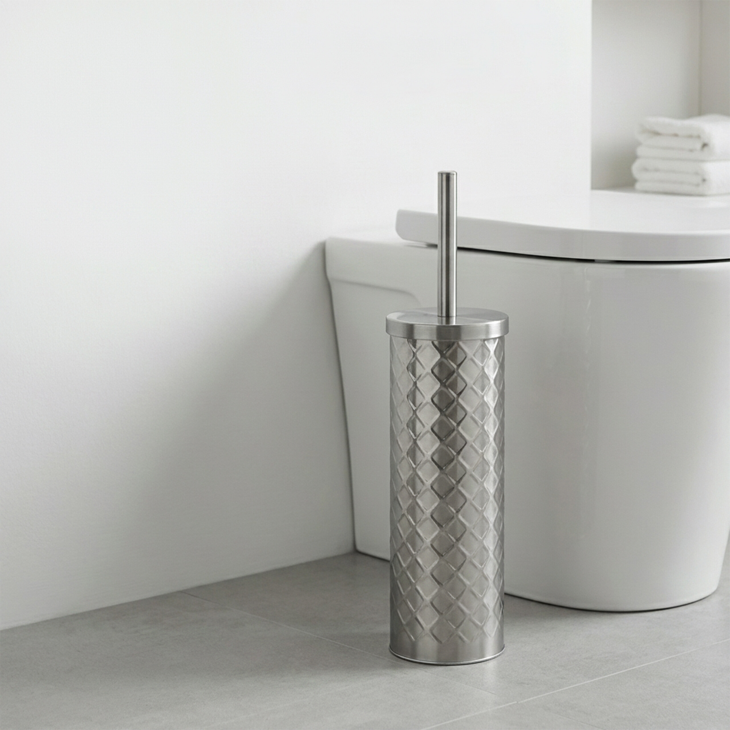 Ein edelstafener Toilettenbürstenhalter mit Rautenmuster steht auf grauem Boden neben einer weißen Toilette.