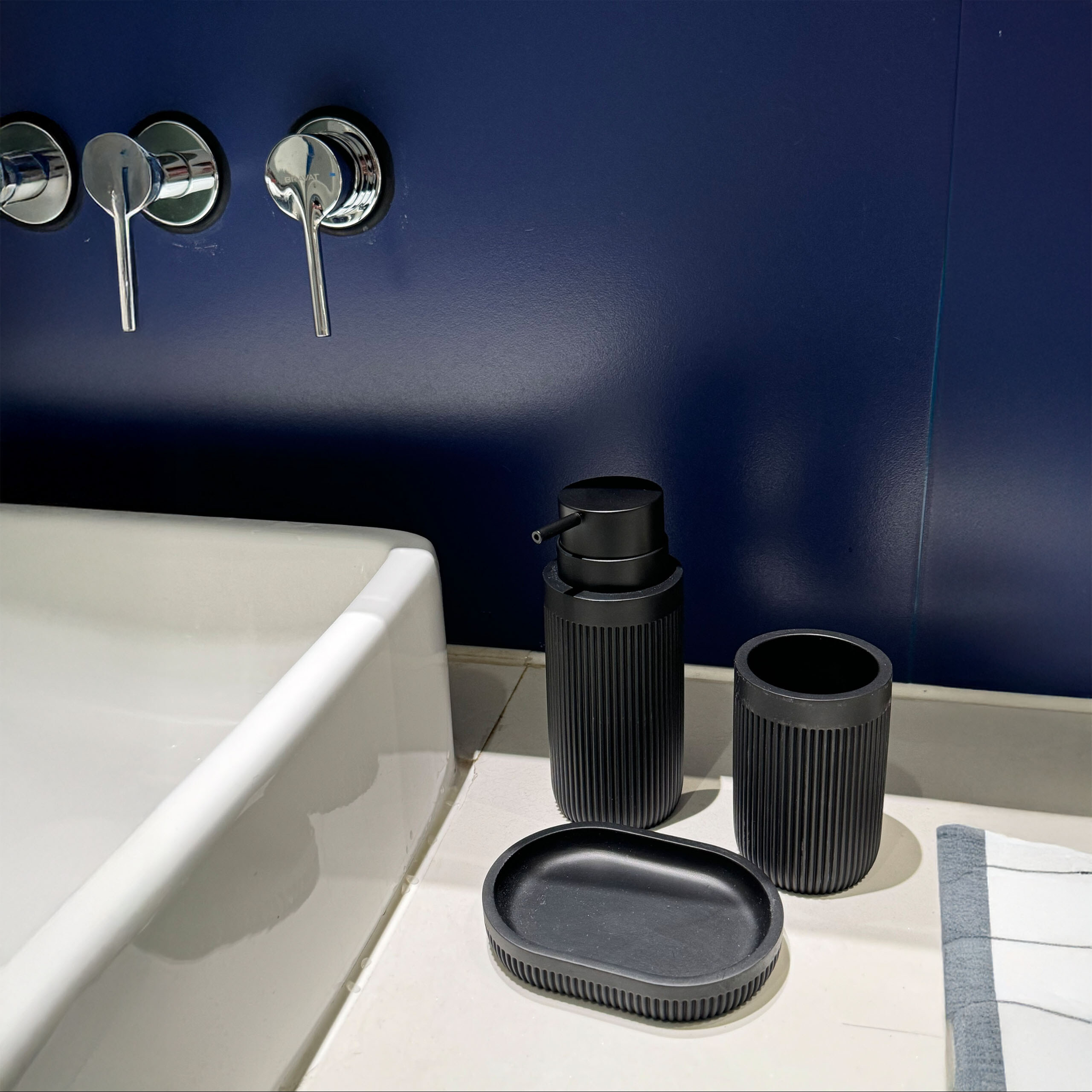 Schwarze Badaccessoires, Seifenspender und ein weißes Waschbecken vor blauer Wand.