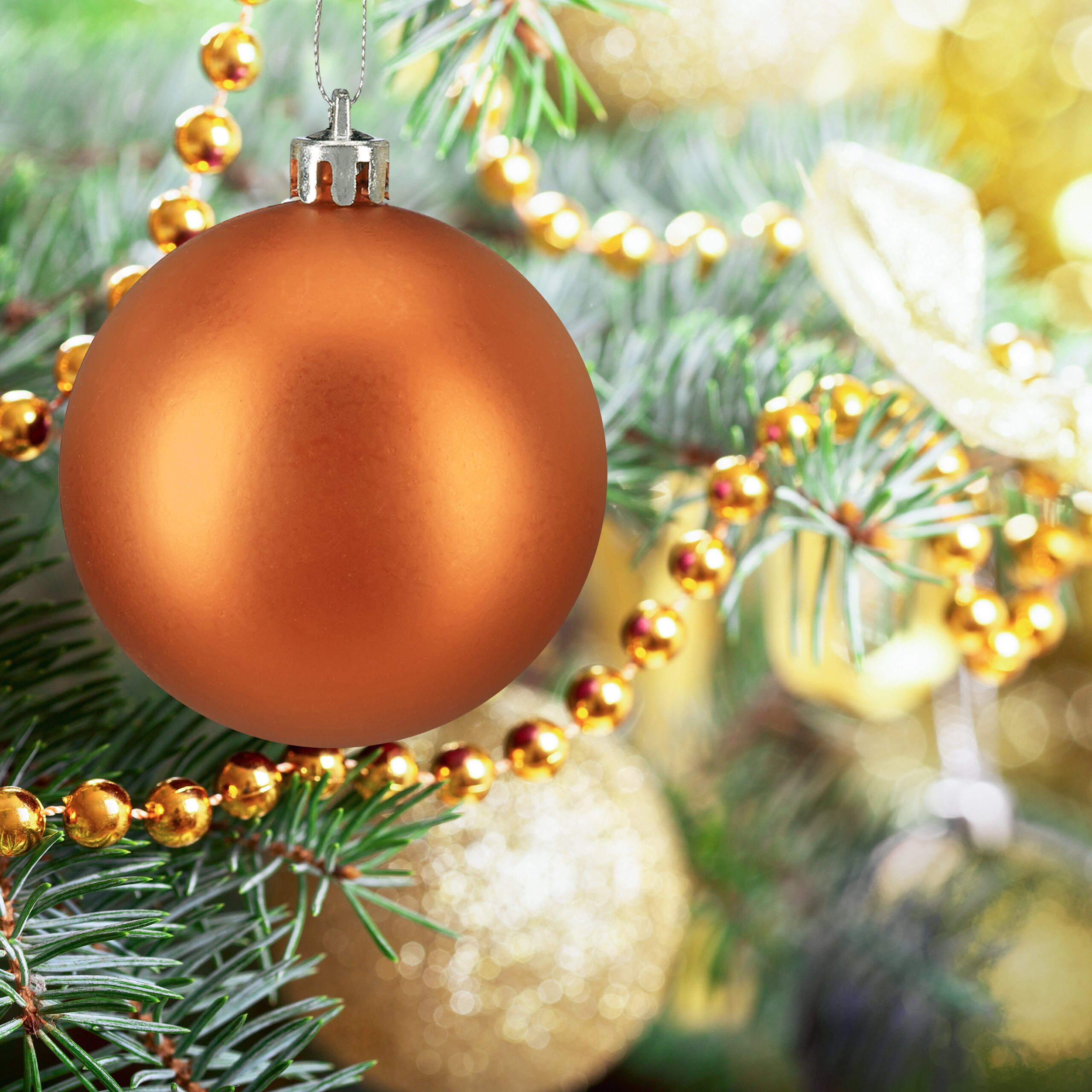 Eine matte orange Christbaumkugel hängt an einem grünen Weihnachtsbaum, umgeben von goldenen Perlenketten und Lichtern.