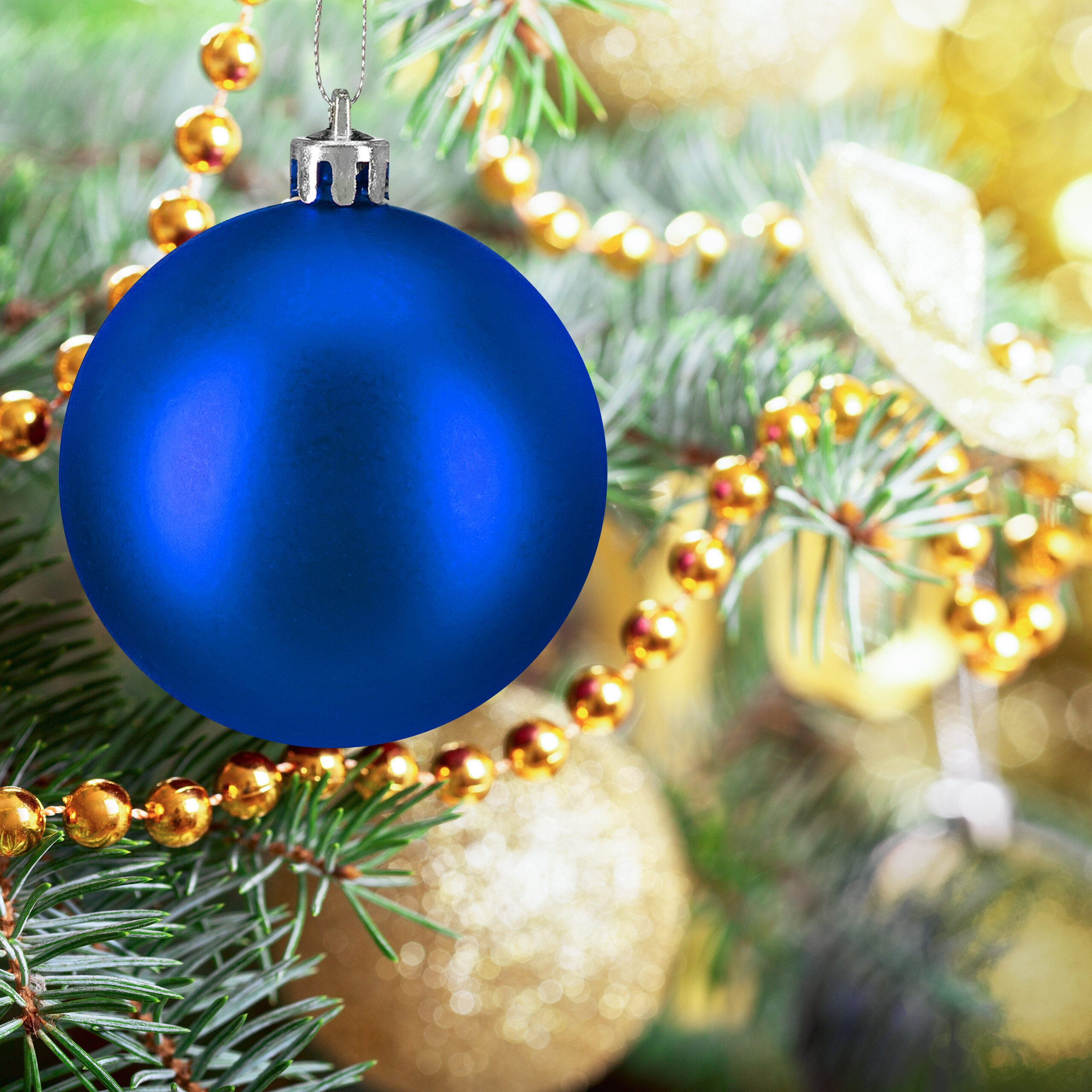 Eine glänzende blaue Weihnachtskugel hängt an einem Tannenbaumzweig mit Goldperlen und Lichtern im Hintergrund.