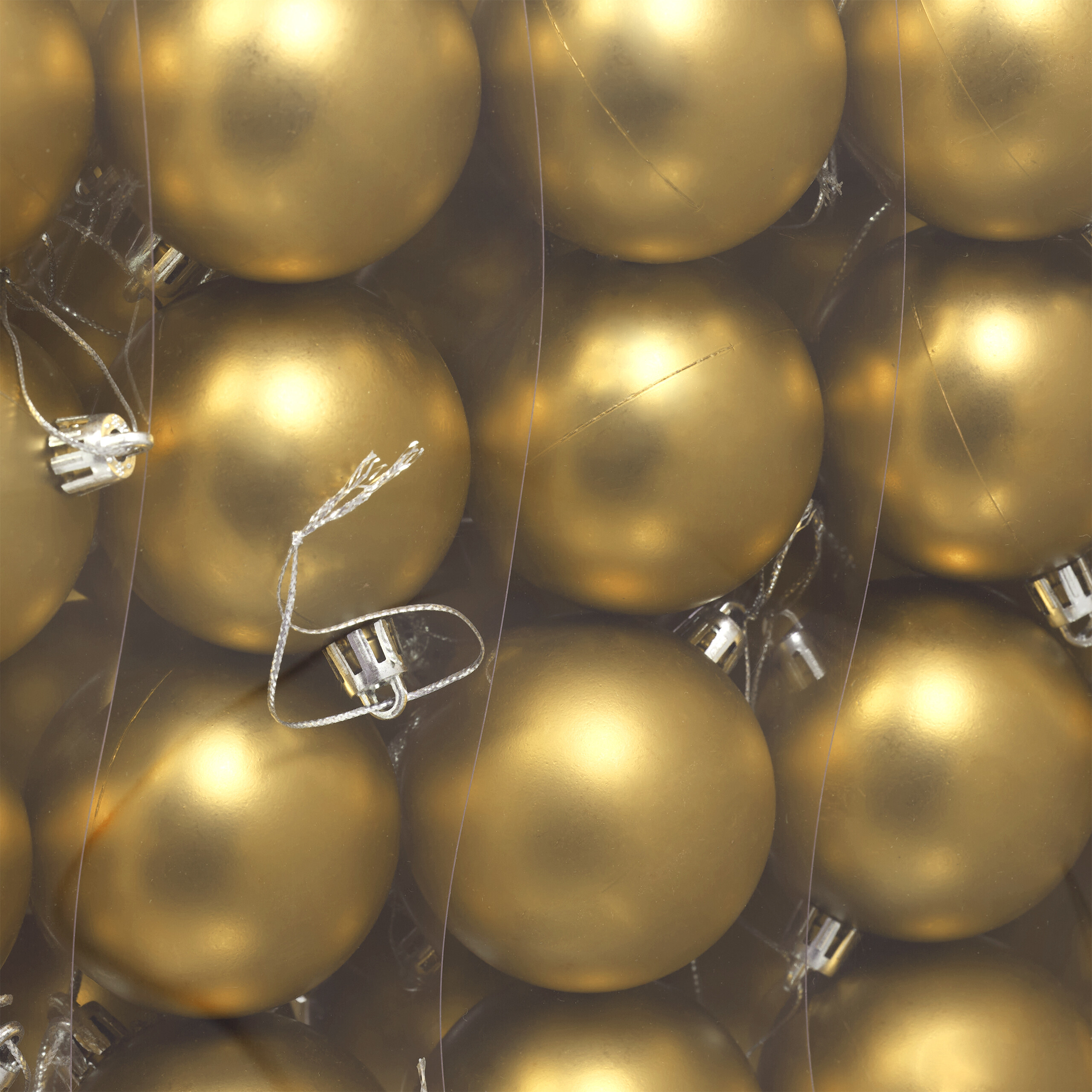 Eine Nahaufnahme vieler glänzender goldener Weihnachtskugeln, verpackt in einer durchsichtigen Schachtel mit silbernen Kappen und Schnüren.