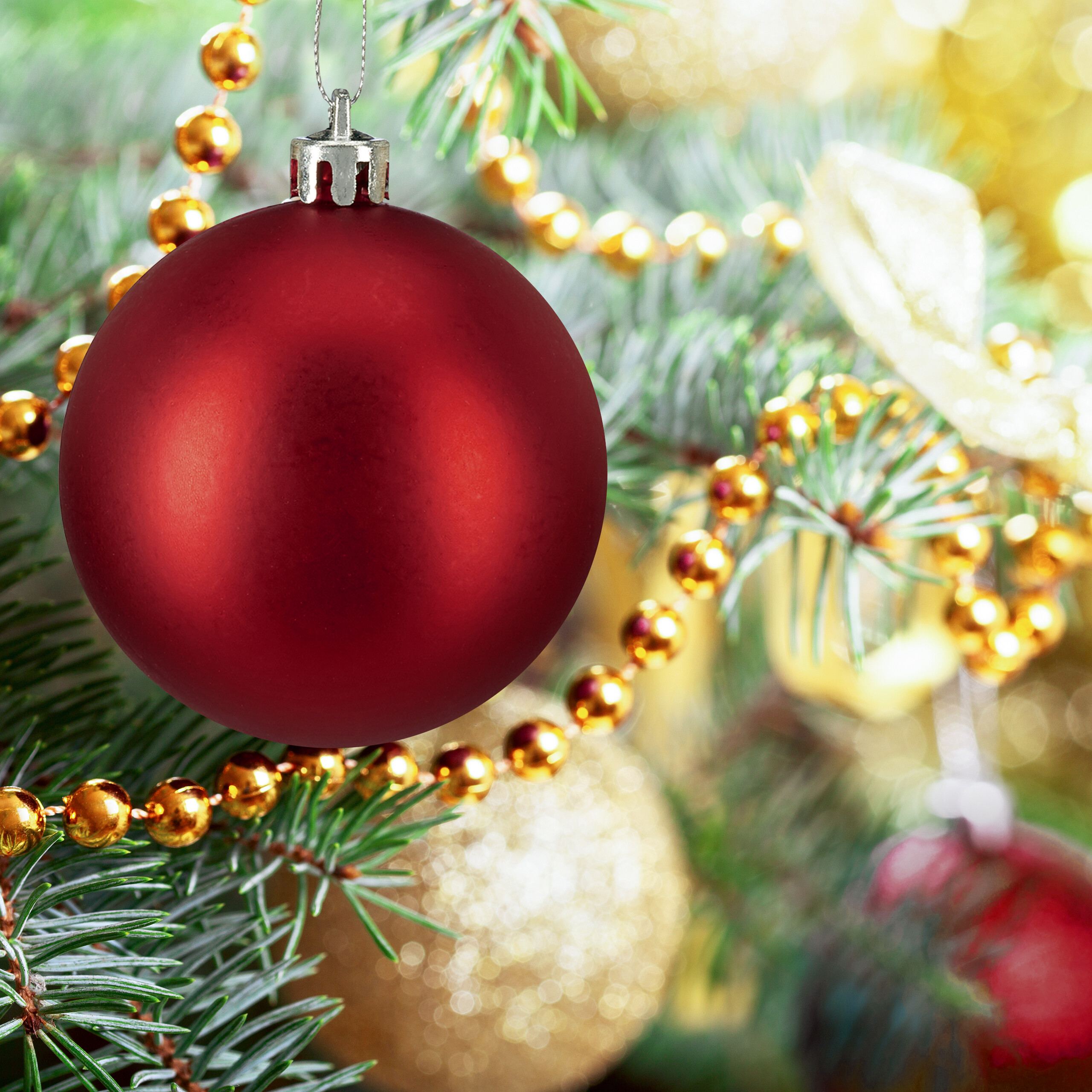Eine große rote Weihnachtskugel hängt an einem grünen Tannenbaum mit Goldperlen.