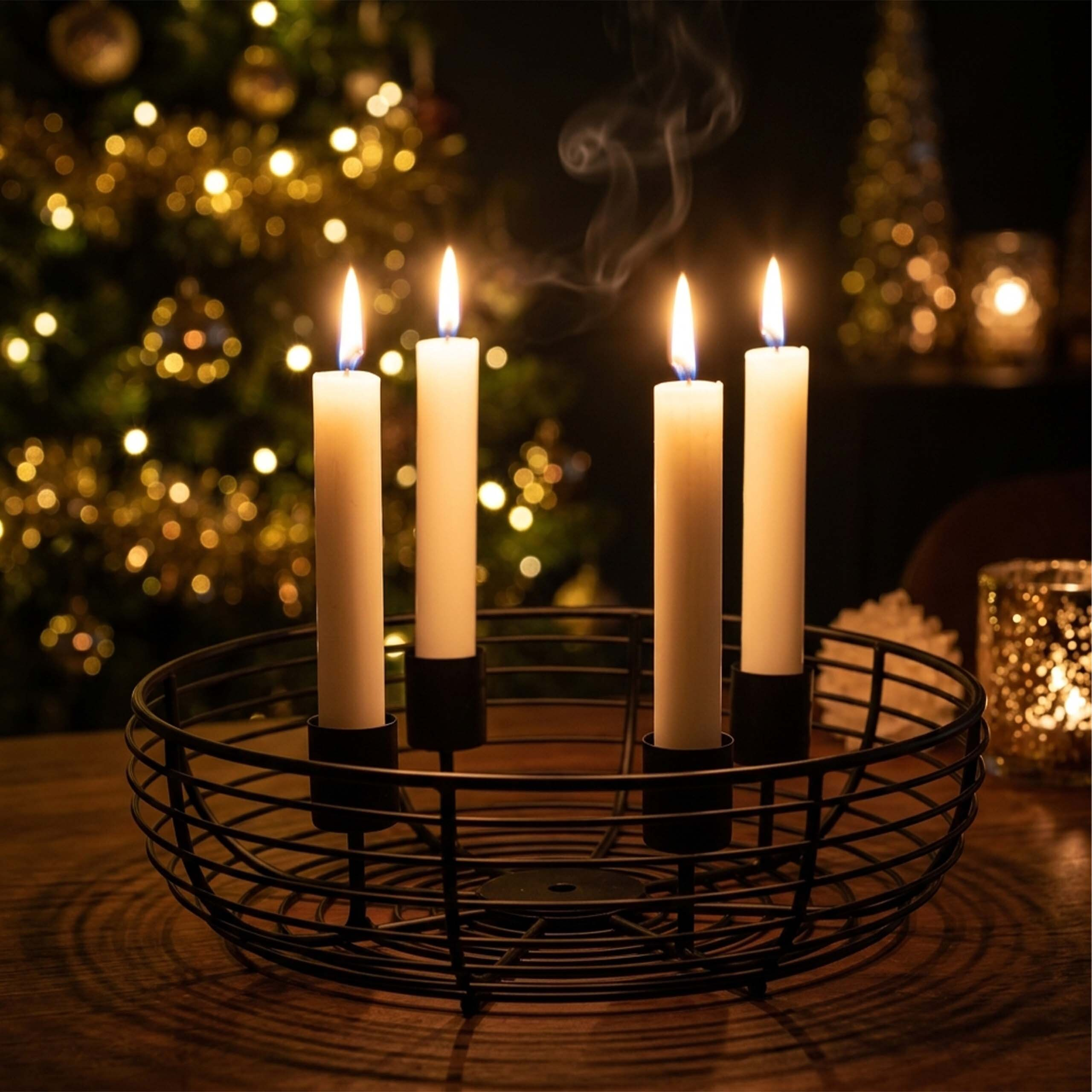 Vier weiße Kerzen brennen in einem schwarzen Drahtkorb vor einem Weihnachtsbaum.