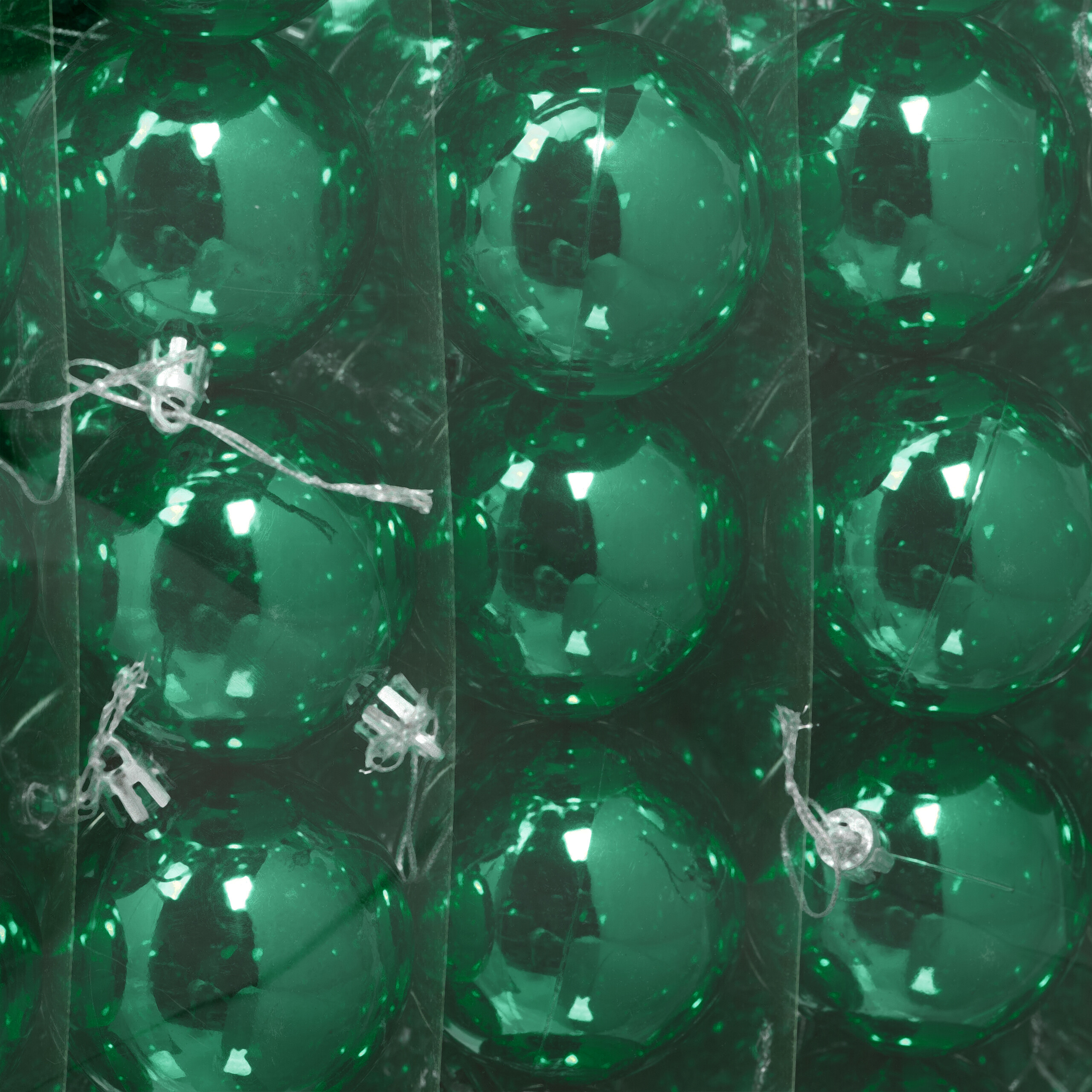 Nahaufnahme glänzender grüner Weihnachtskugeln, dicht verpackt in durchsichtiger Plastikverpackung.