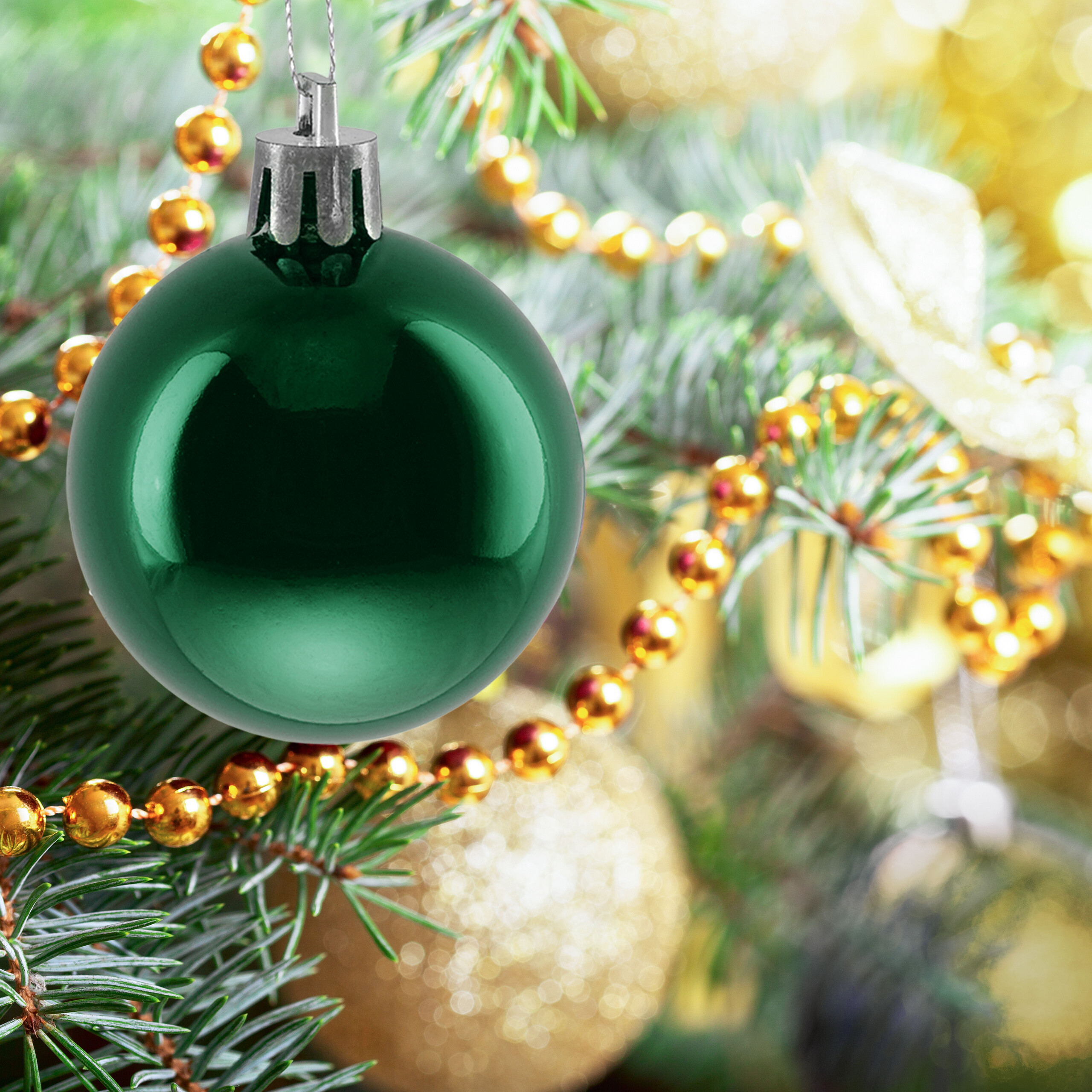 Eine glänzende grüne Weihnachtskugel hängt an einem geschmückten Weihnachtsbaum mit goldenen Perlen.