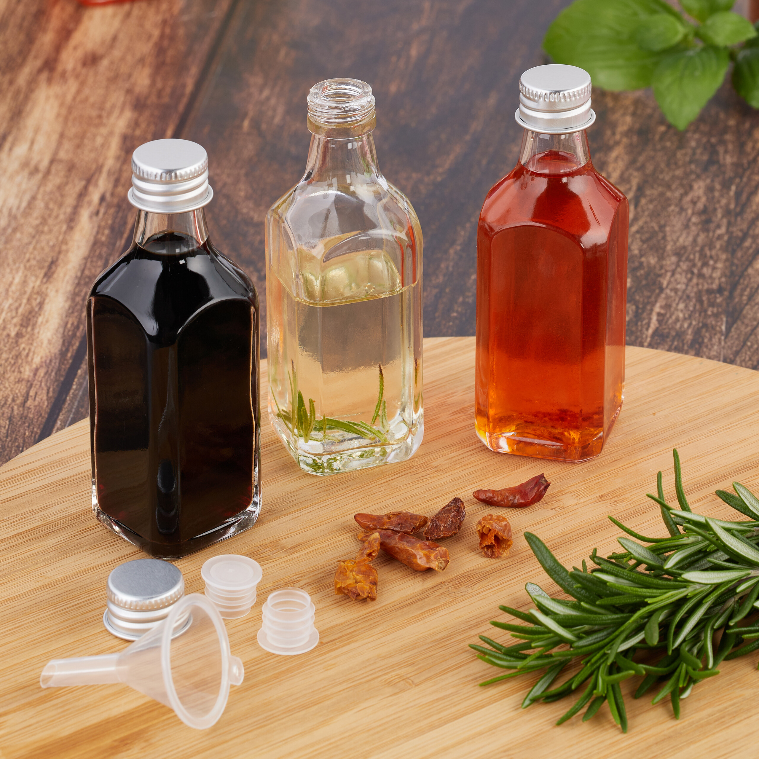 Drei Glasflaschen mit dunkler, klarer und roter Flüssigkeit auf einem Holzbrett mit Chilischoten und Rosmarin.