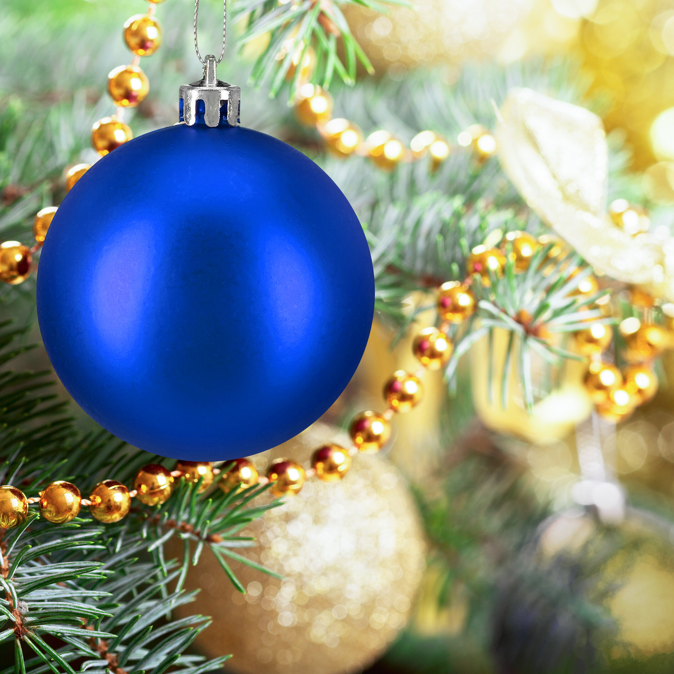 Eine blaue Weihnachtskugel hängt an einem Weihnachtsbaum mit goldenen Perlenketten.
