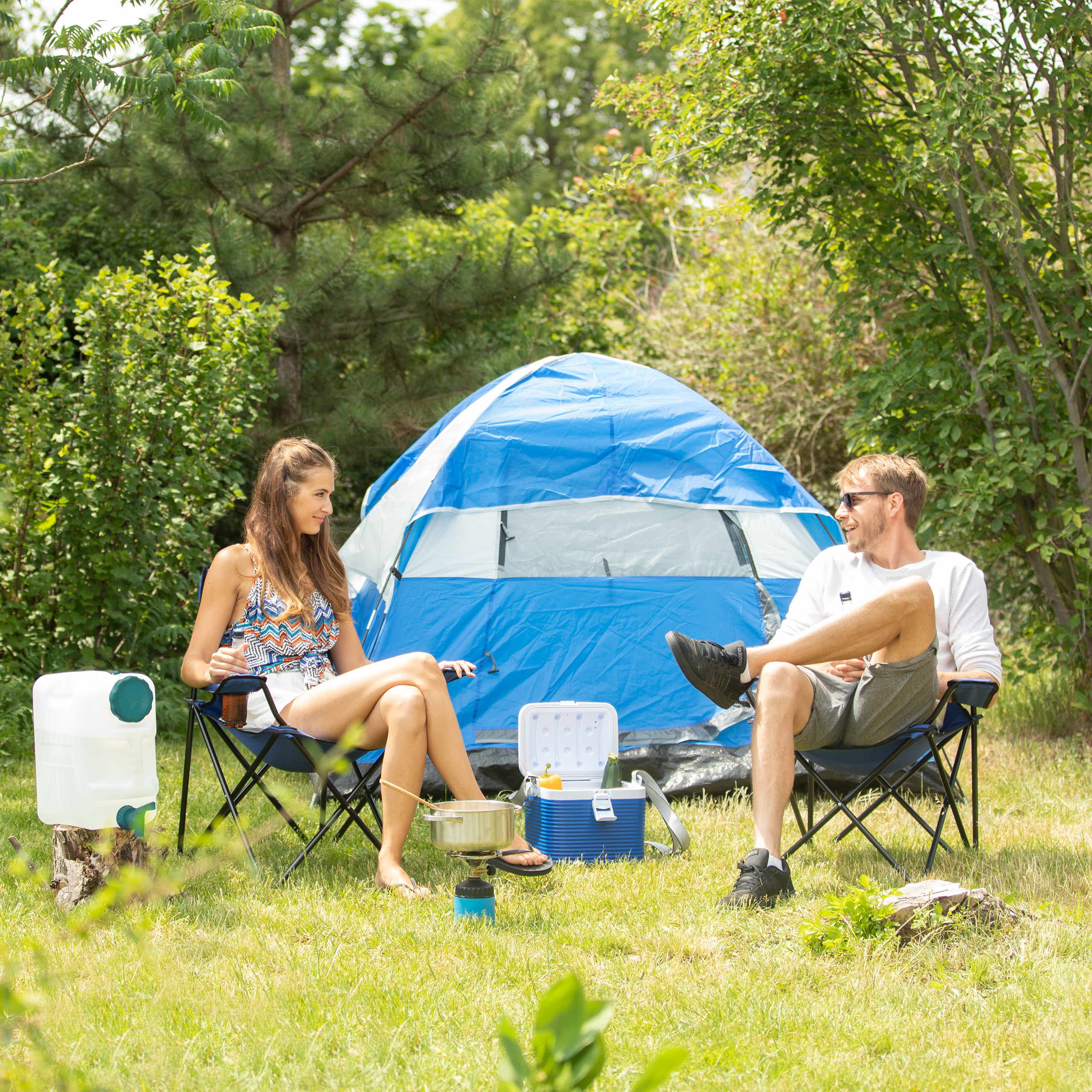 Ein Paar sitzt vor einem blauen Zelt in der Natur und campen.