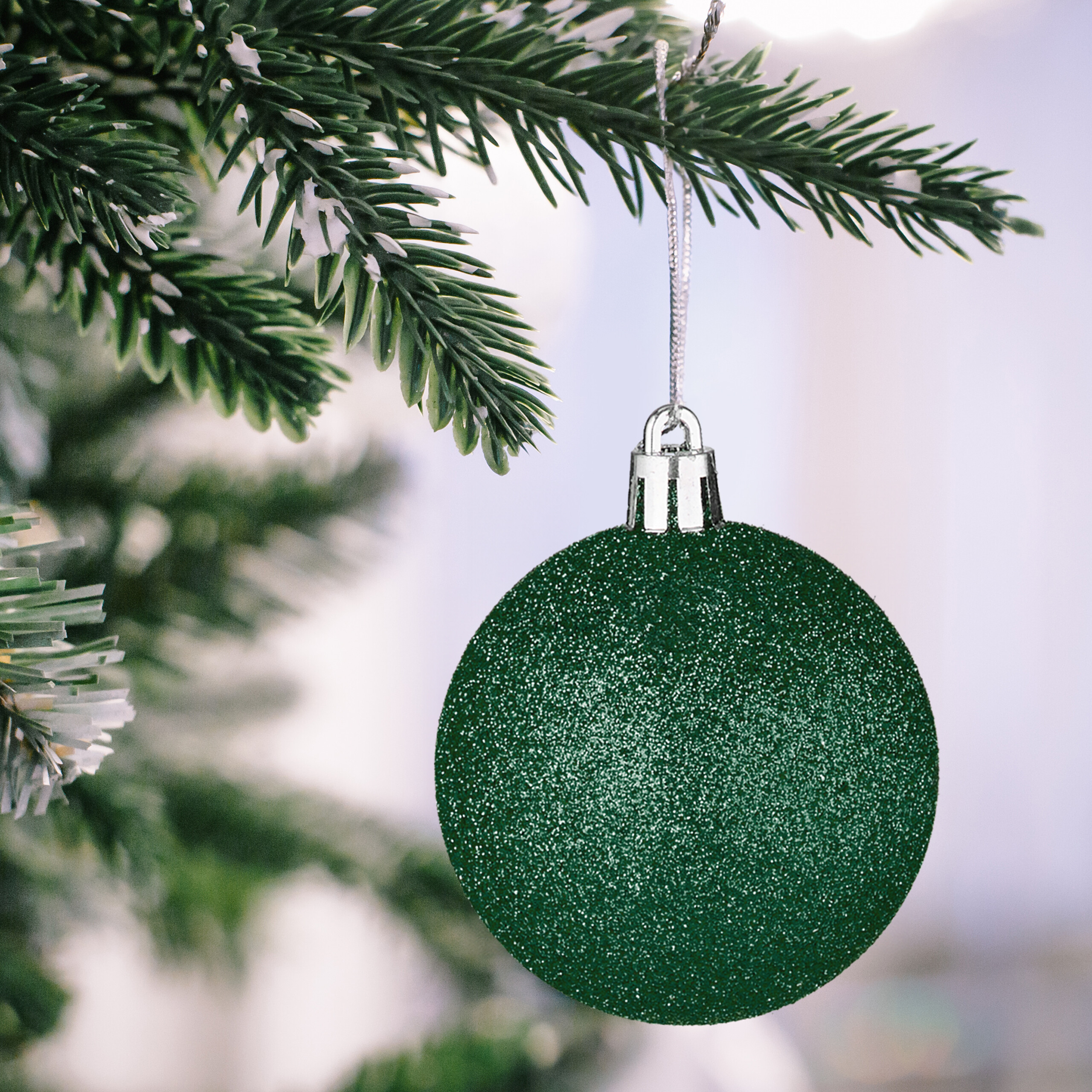 Glänzende grüne Weihnachtskugel hängt an einem verschneiten Weihnachtsbaumzweig.