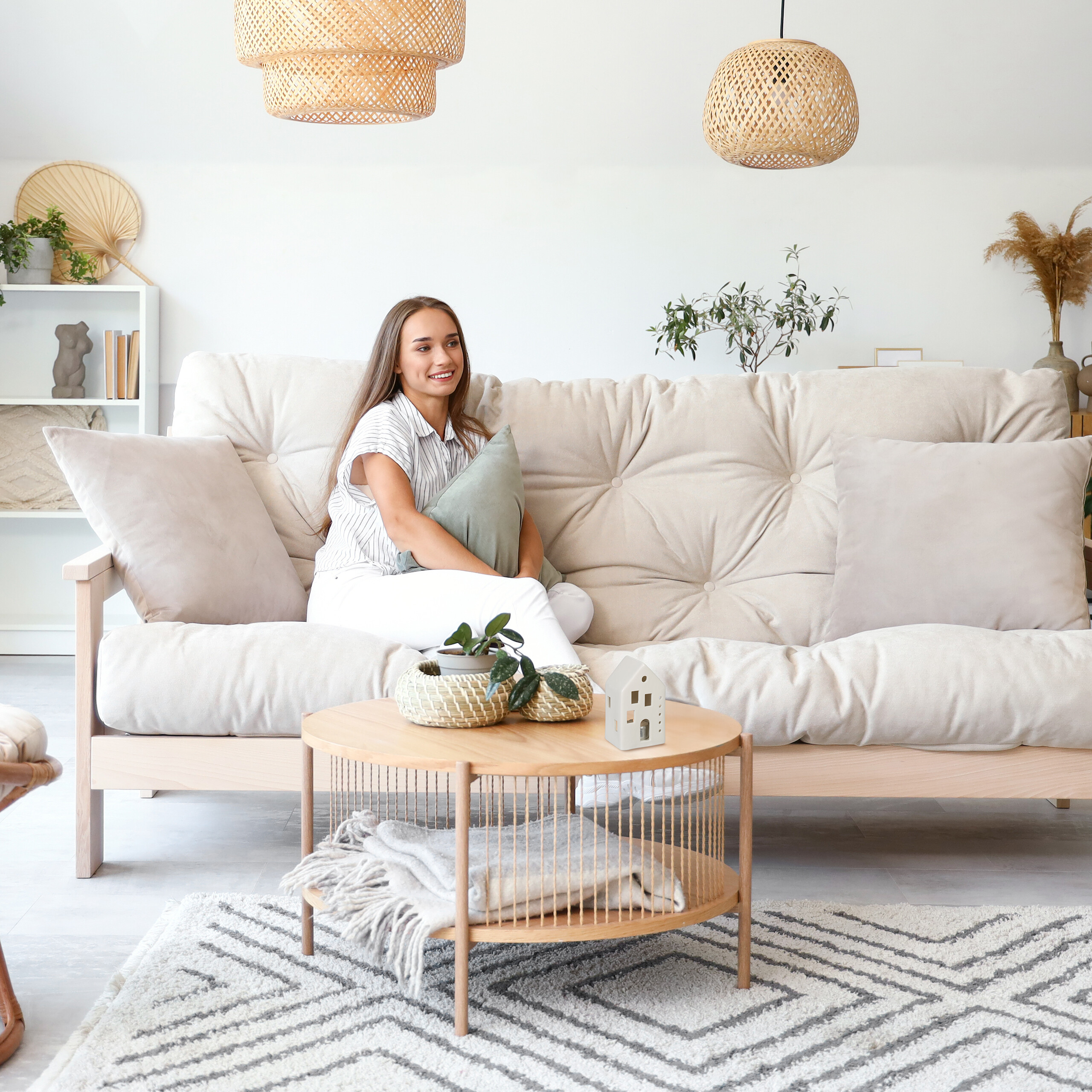 Eine Frau sitzt auf einem hellen Sofa im Wohnzimmer vor einem runden Holztisch.
