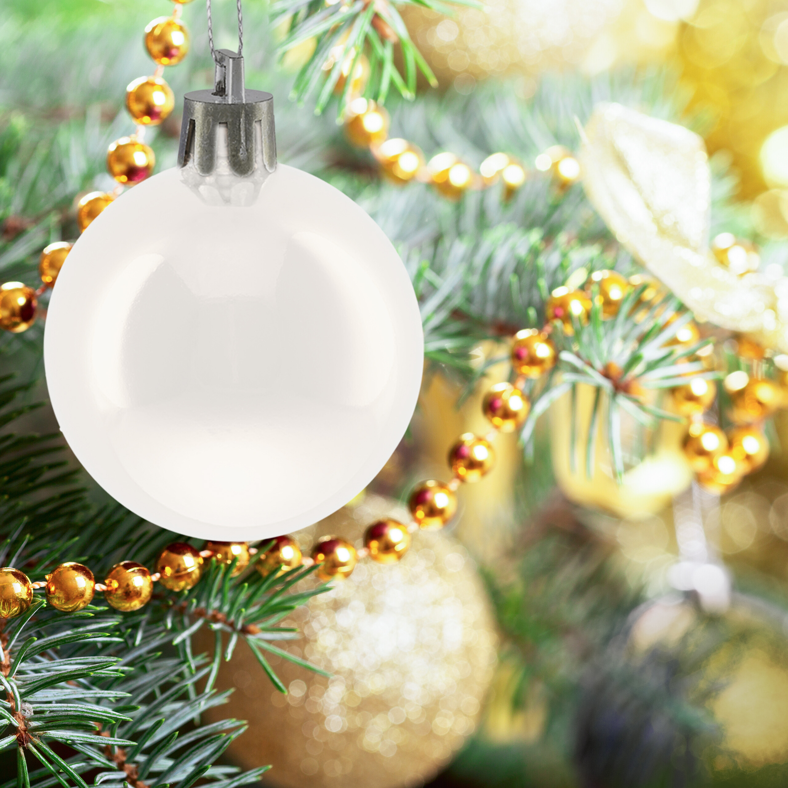 Eine weiße Weihnachtskugel hängt an einem Tannenbaumzweig mit goldenen Perlenketten.