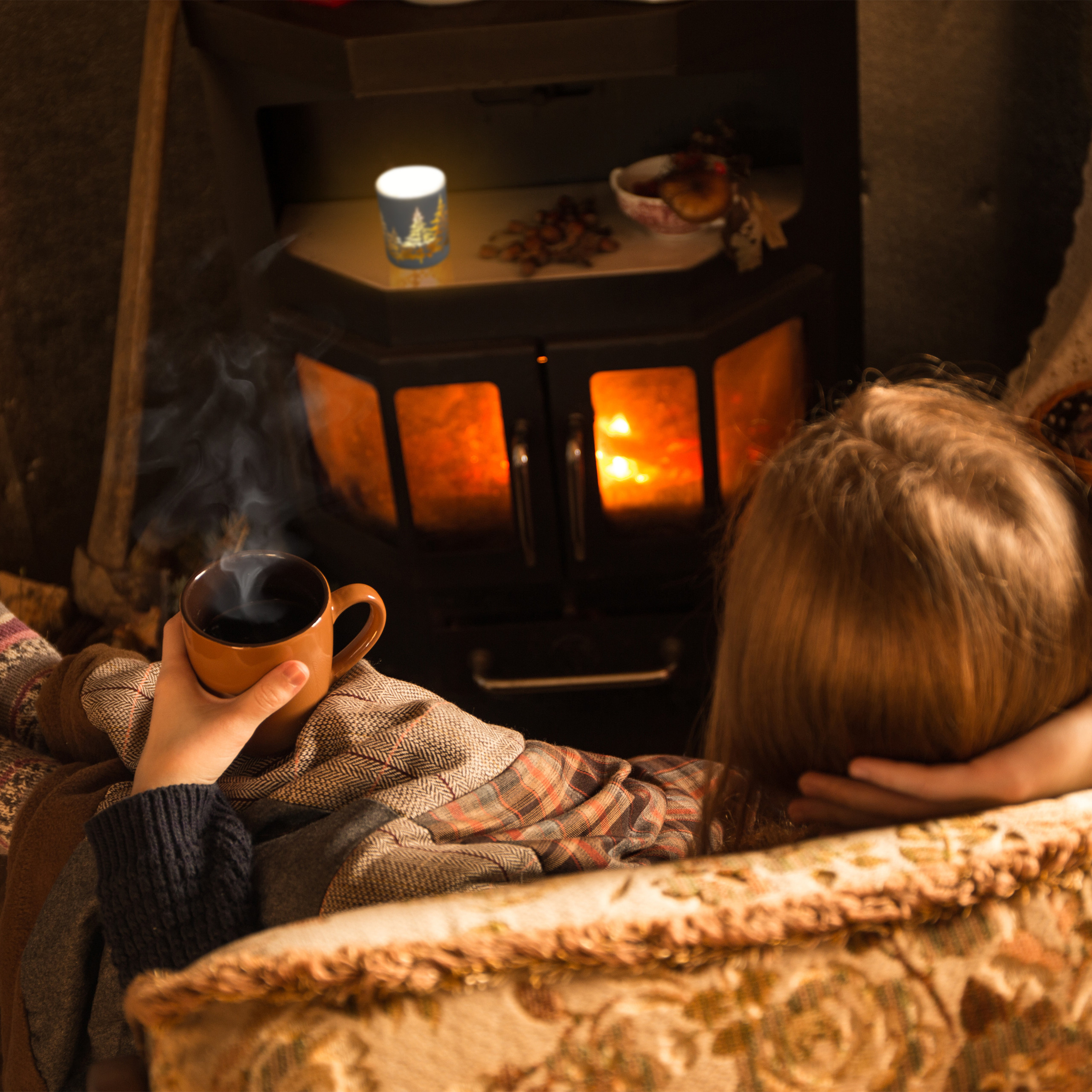 Eine Person sitzt gemütlich vor einem warmen Kamin und hält eine Tasse heißen Kaffee.