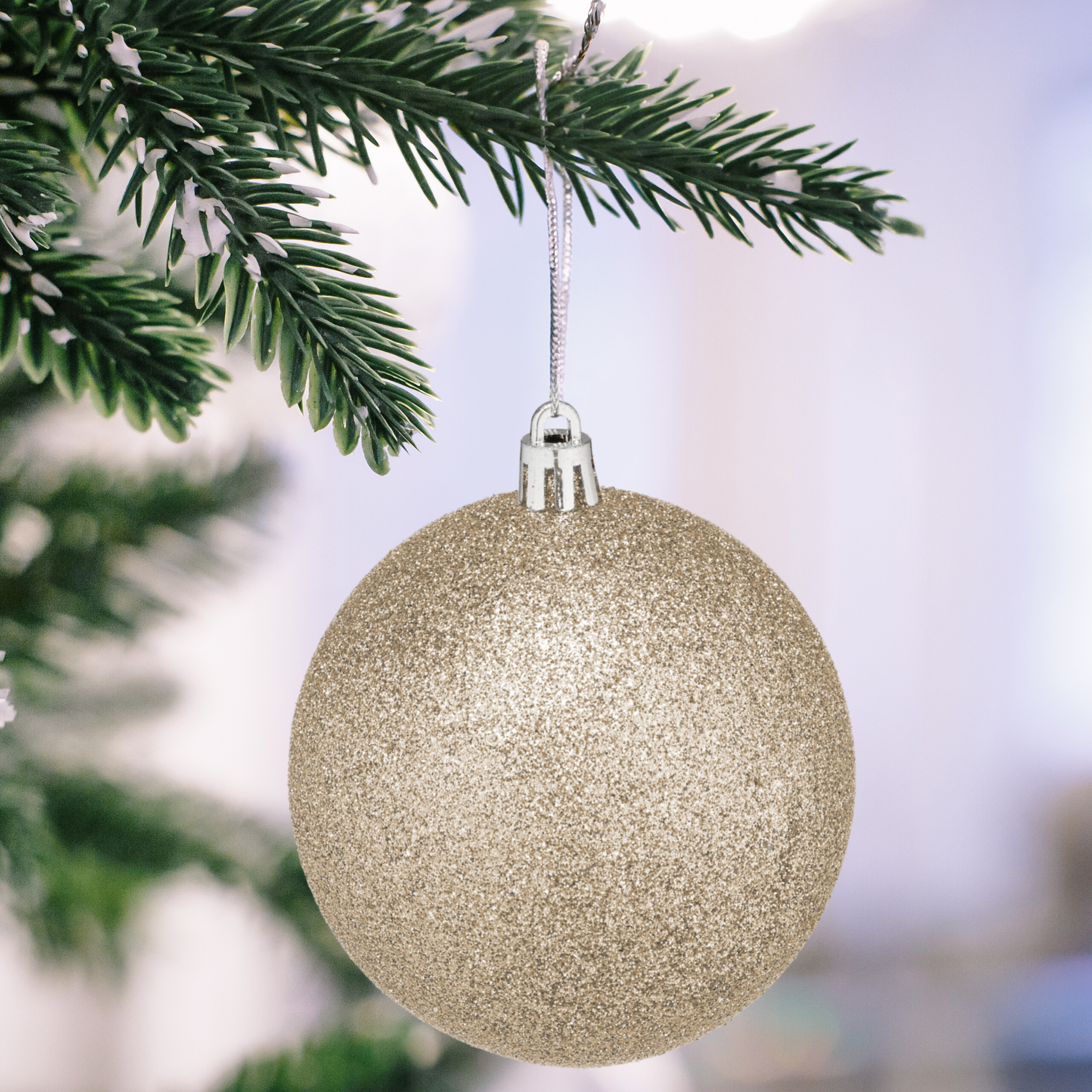 Eine glitzernde goldene Weihnachtskugel hängt an einem verschneiten Weihnachtsbaumzweig.