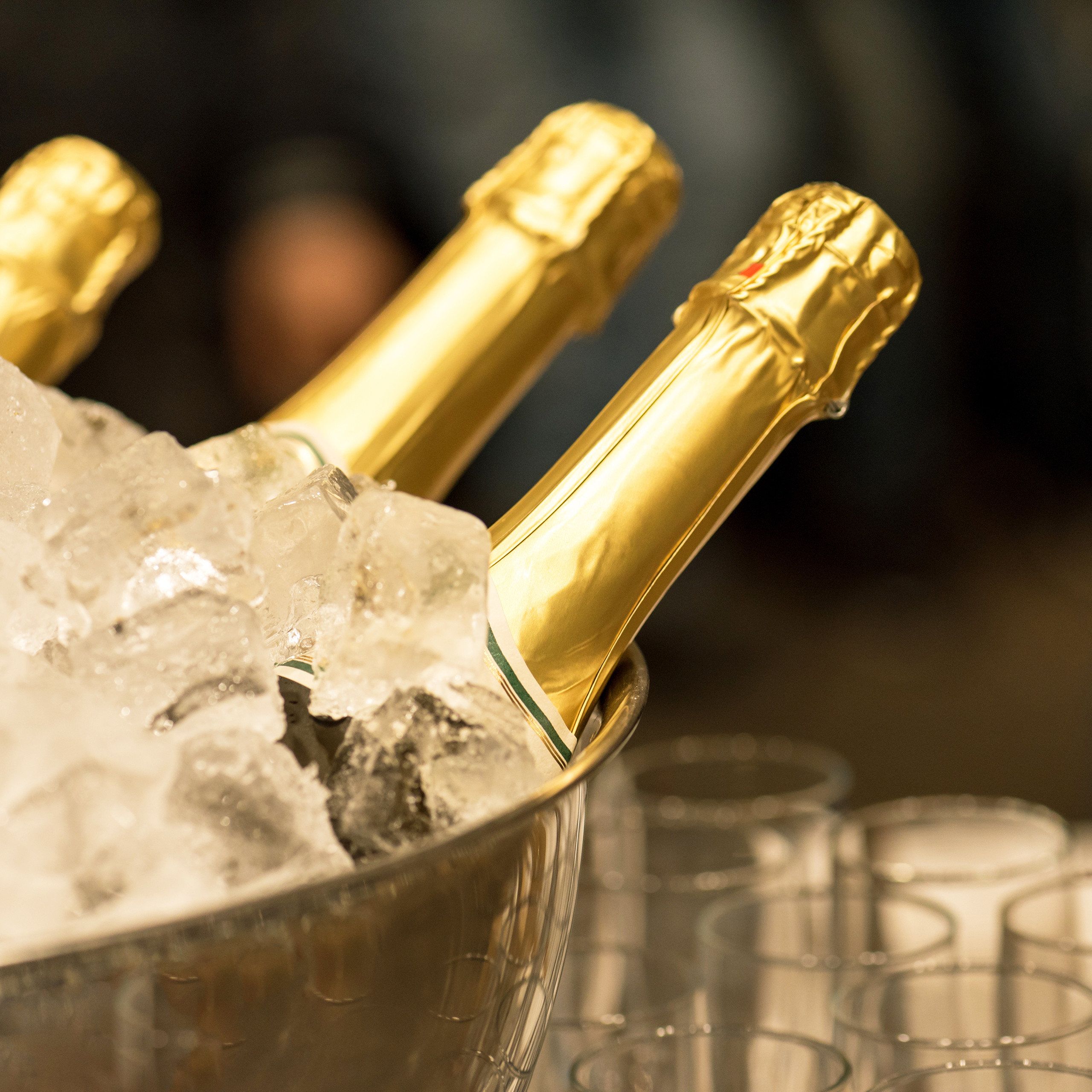 Goldene Champagnerflaschen stecken in einem mit Eis gefüllten Eimer, daneben stehen leere Gläser.