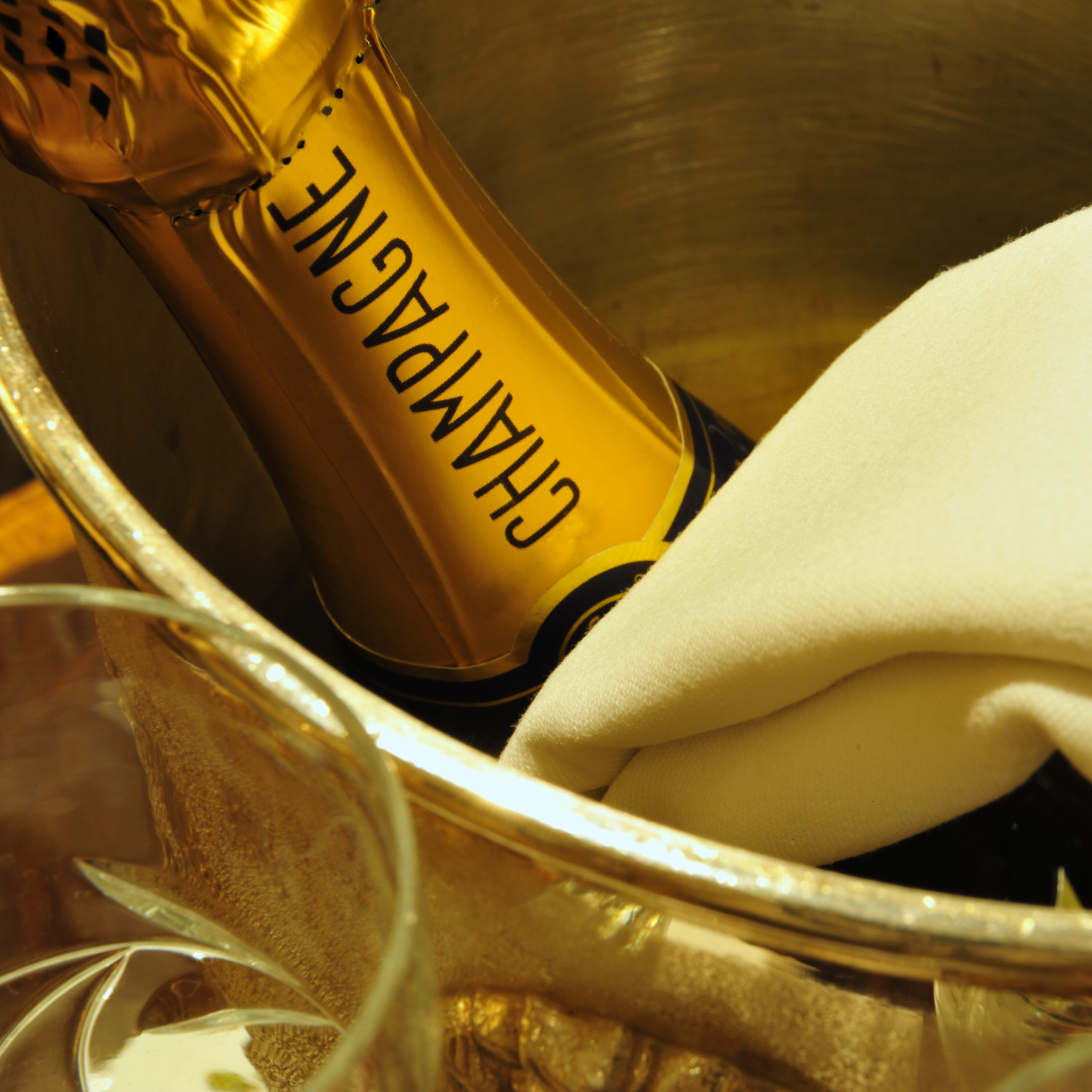 Eine Champagnerflasche in einem Eiskübel mit einer weißen Serviette und einem leeren Glas im Vordergrund.