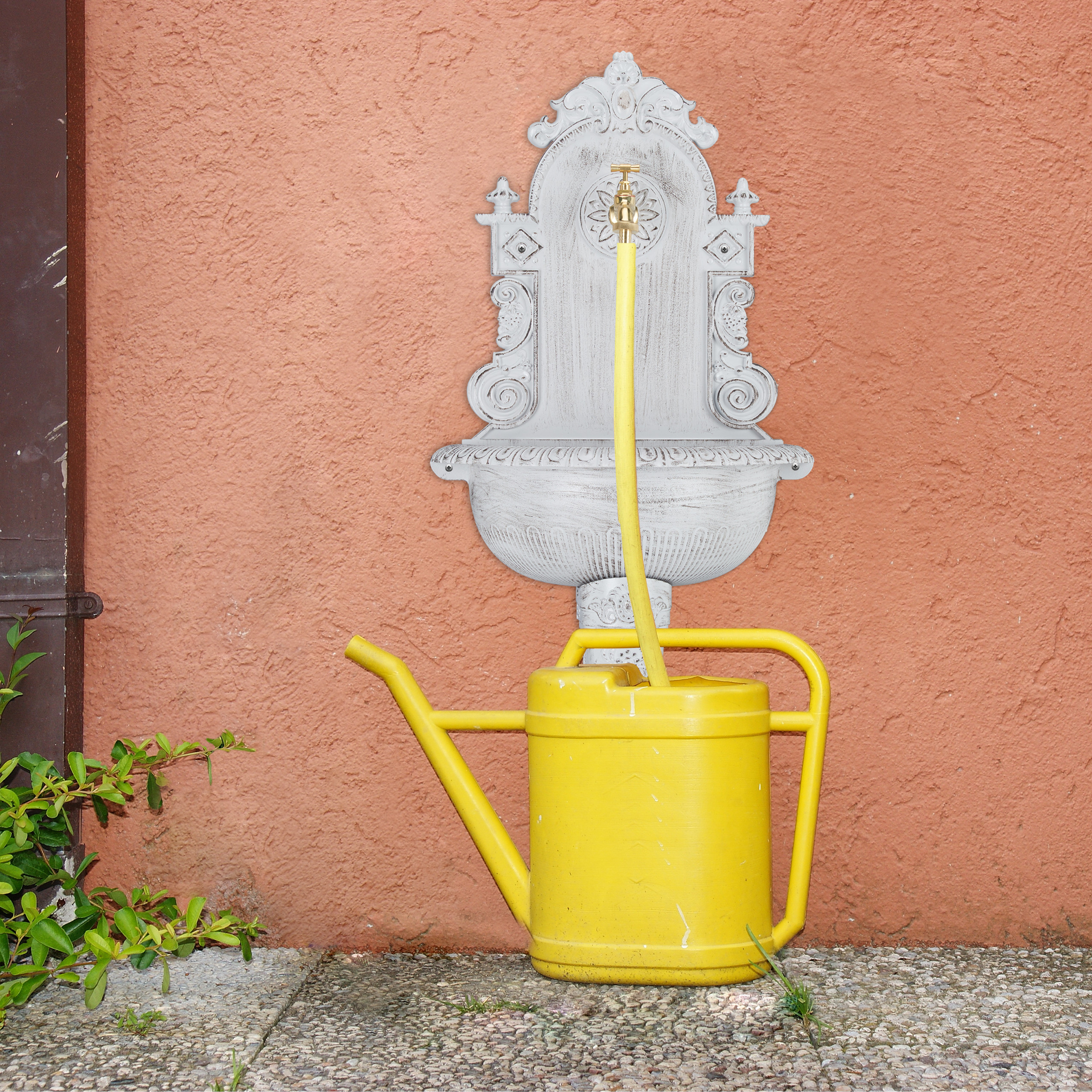 Eine weiße Wandbrunnen mit goldenem Wasserhahn und gelber Gießkanne auf orangem Putz.