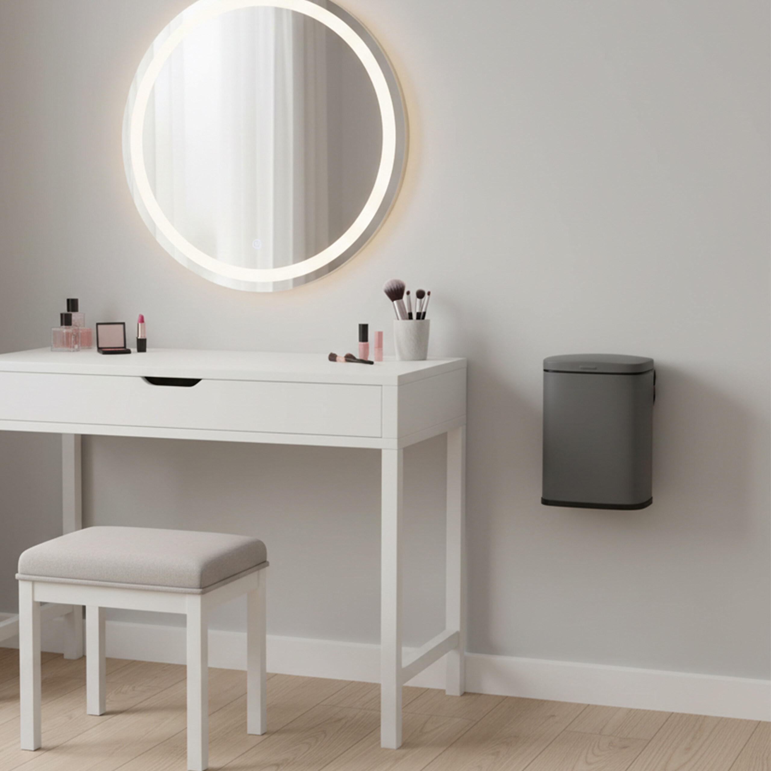Ein weißer Schminktisch mit Hocker und rundem Spiegel, daneben hängt ein grauer Mülleimer an der Wand.