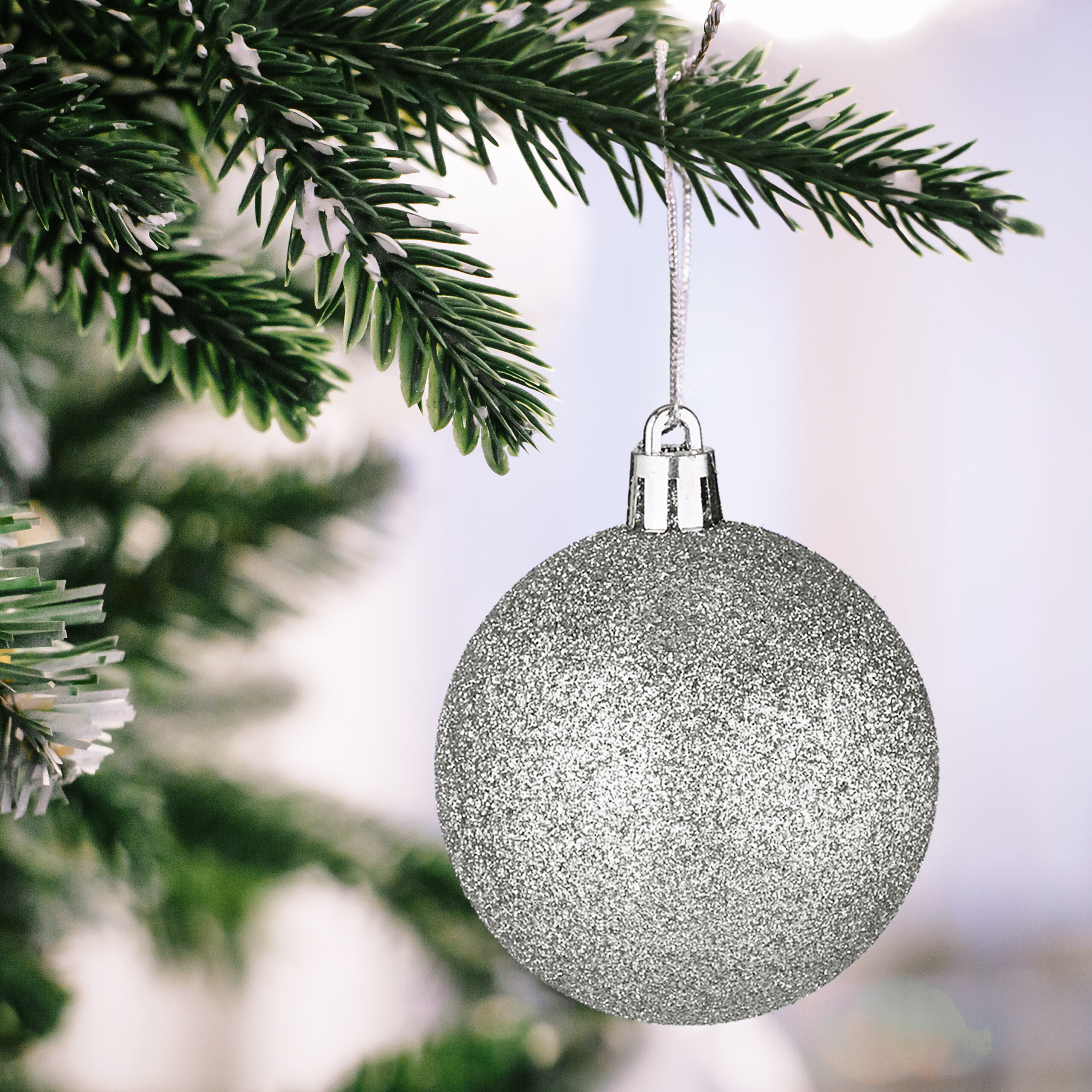 Eine funkelnde silberne Weihnachtskugel hängt an einem grünen Zweig.