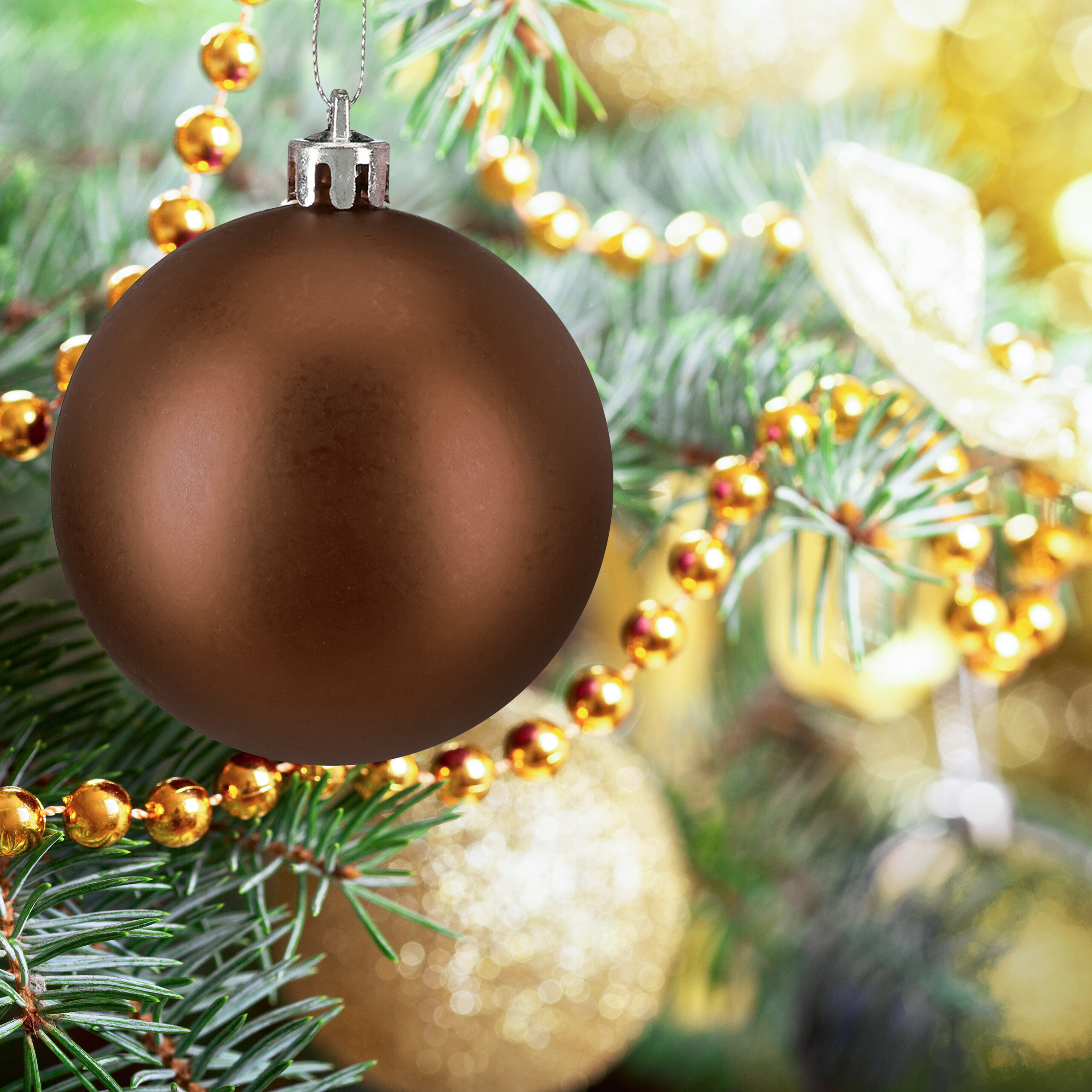 Eine matte braune Weihnachtskugel hängt an einem Weihnachtsbaum mit goldenen Perlen und Lichtern.