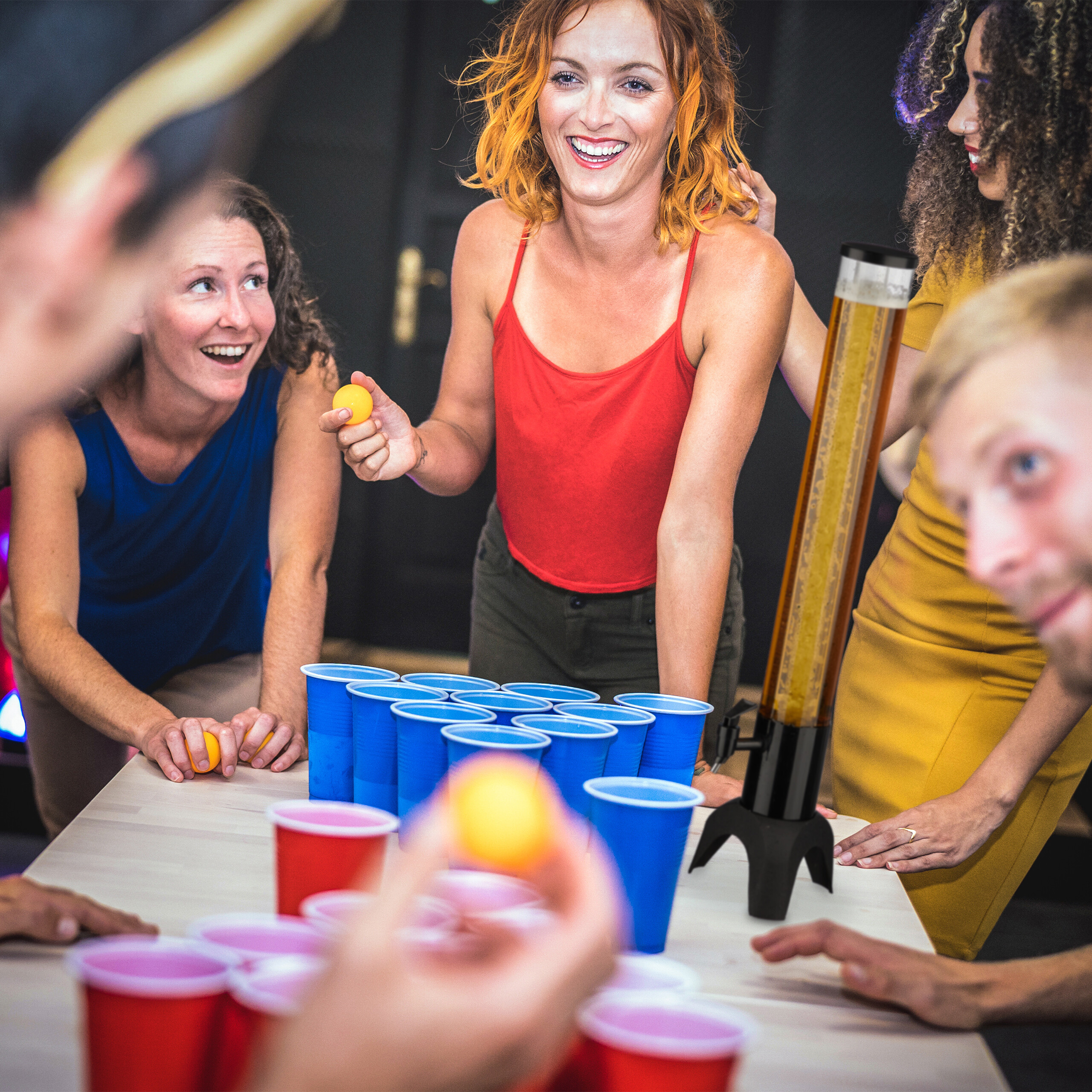Freunde spielen Beer Pong mit blauen und roten Bechern auf einem Tisch.