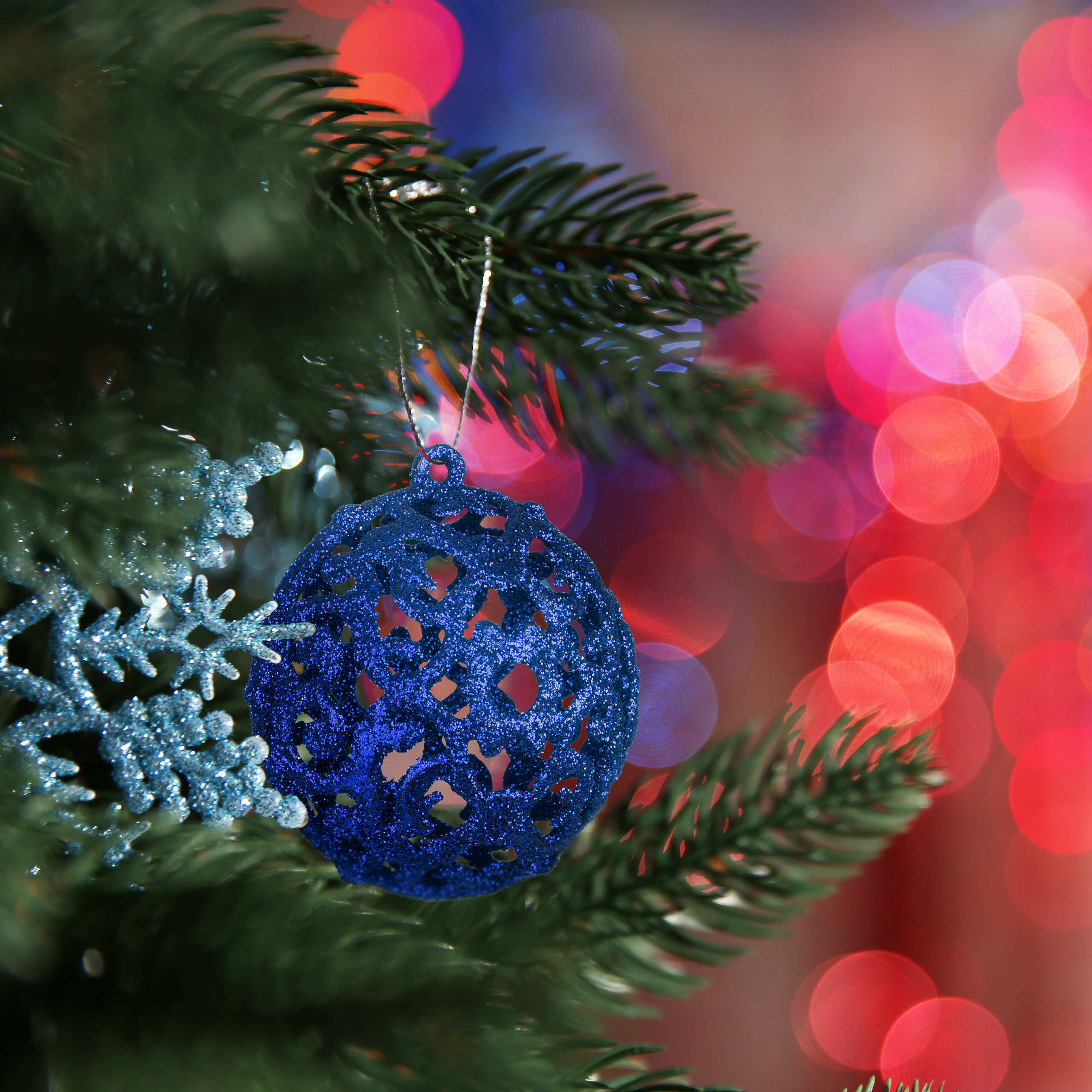 Eine blaue Glaskugel und silberne Schneeflocken hängen an einem Weihnachtsbaum vor verschwommenem Hintergrund.