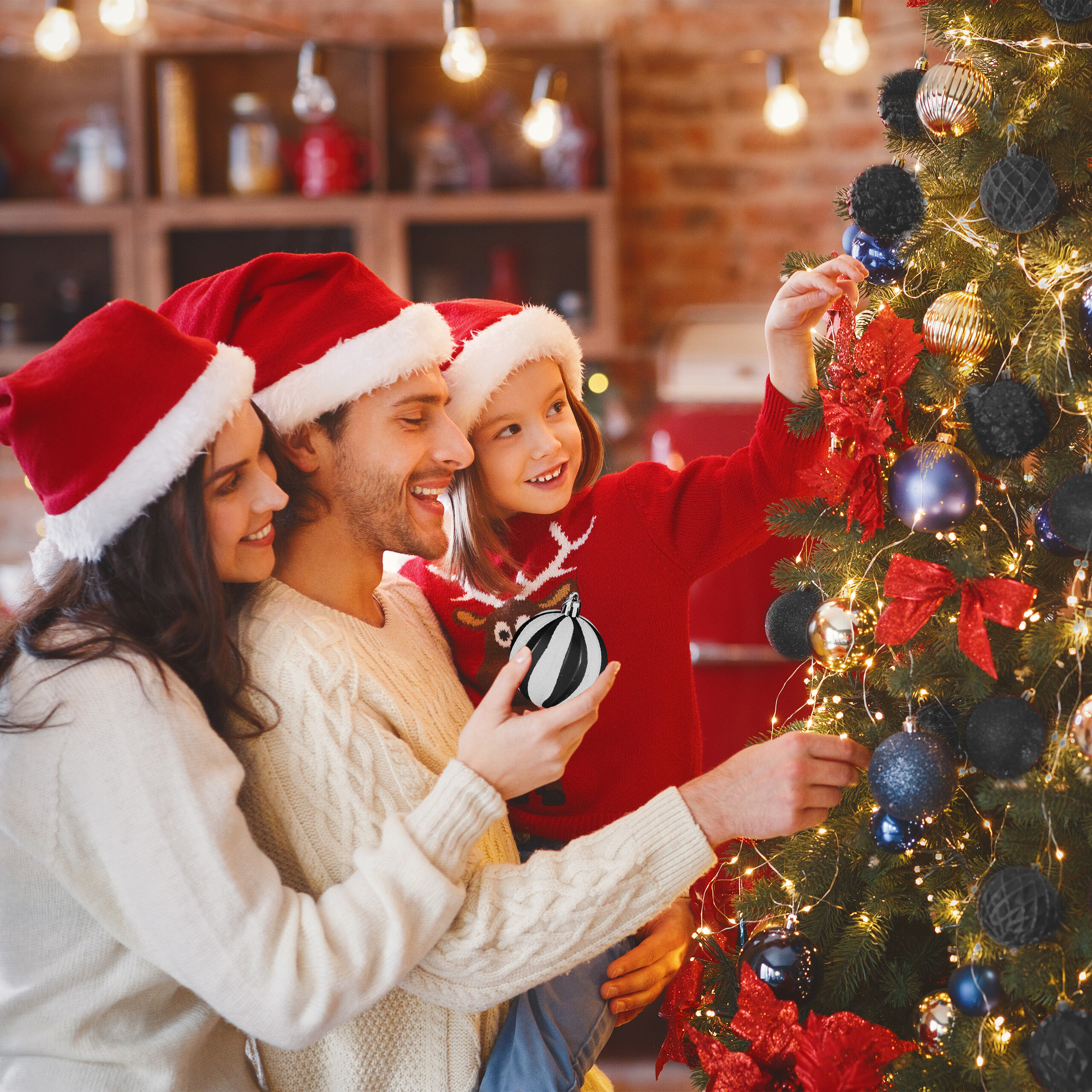Familie mit Weihnachtsmützen schmückt einen hell erleuchteten Weihnachtsbaum in einem gemütlichen Raum.