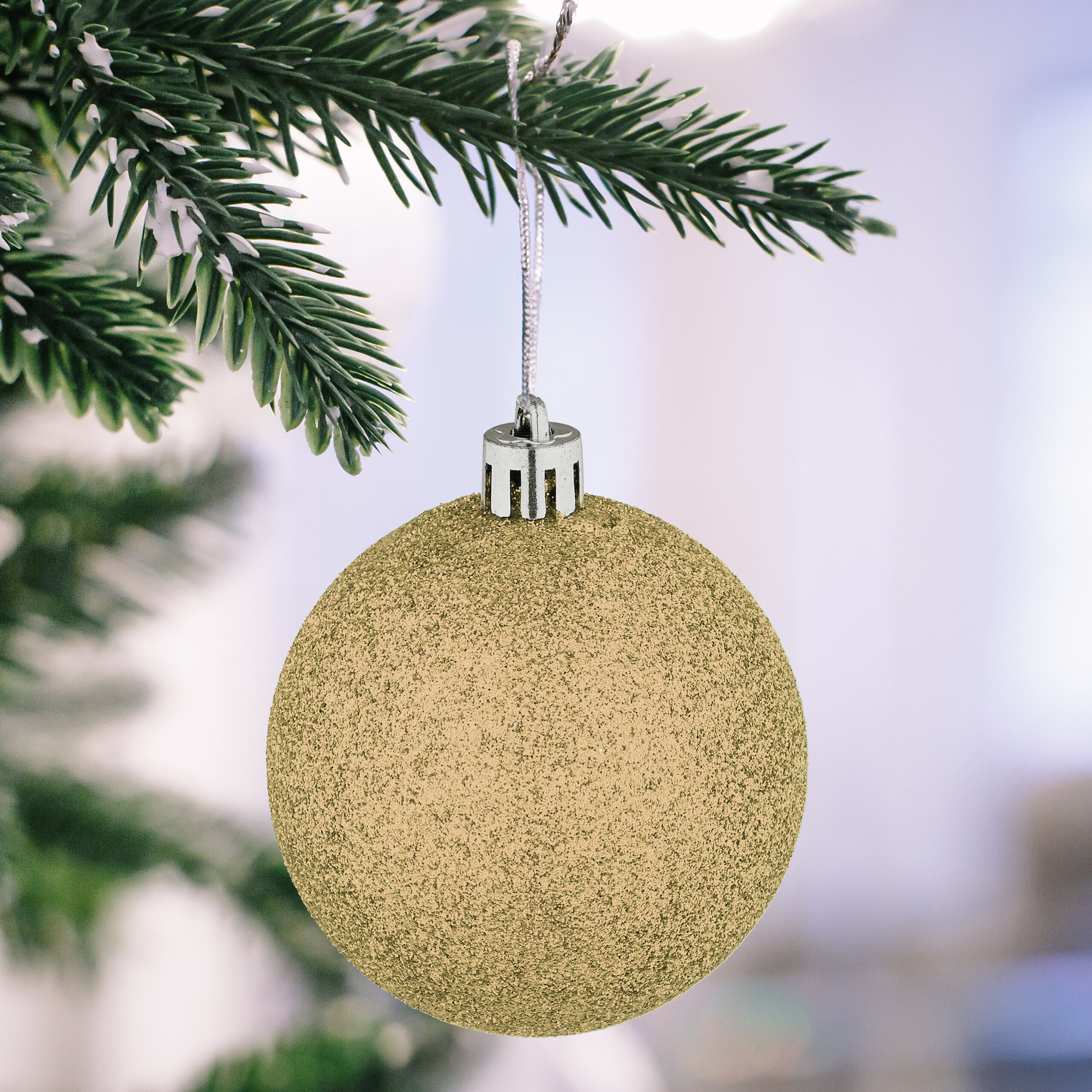 Eine glitzernde goldene Weihnachtskugel hängt an einem verschneiten Tannenzweig.