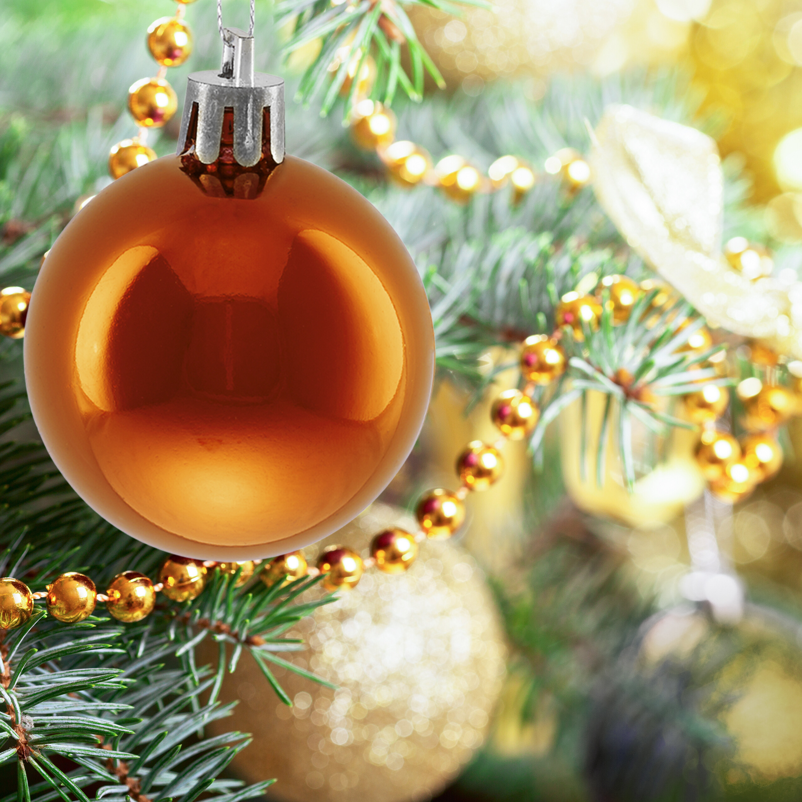 Eine glänzende goldene Weihnachtskugel hängt an einem Tannenbaumzweig mit goldenen Perlenketten.