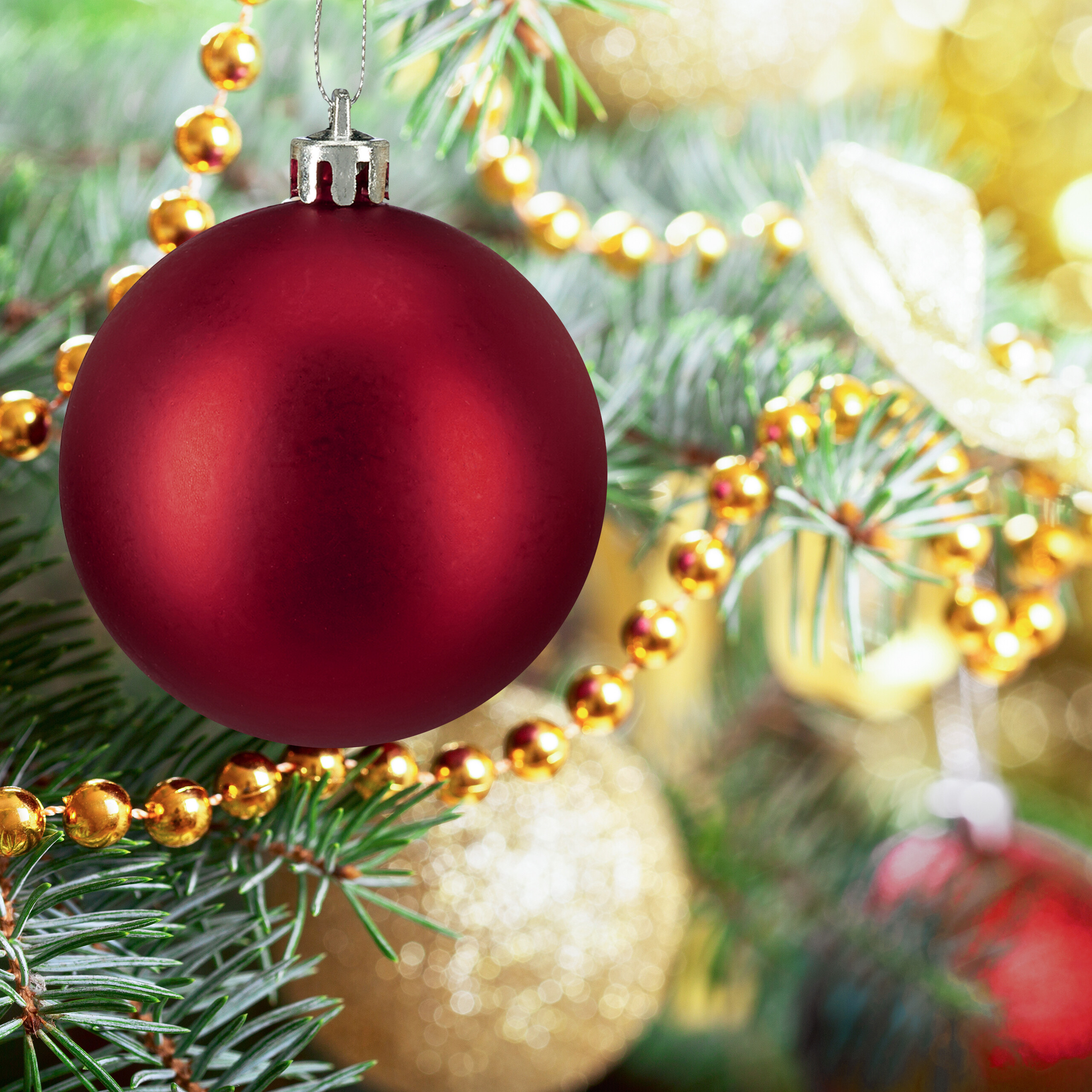 Eine matte rote Weihnachtskugel hängt an einem grünen Weihnachtsbaum, geschmückt mit goldenen Perlen.
