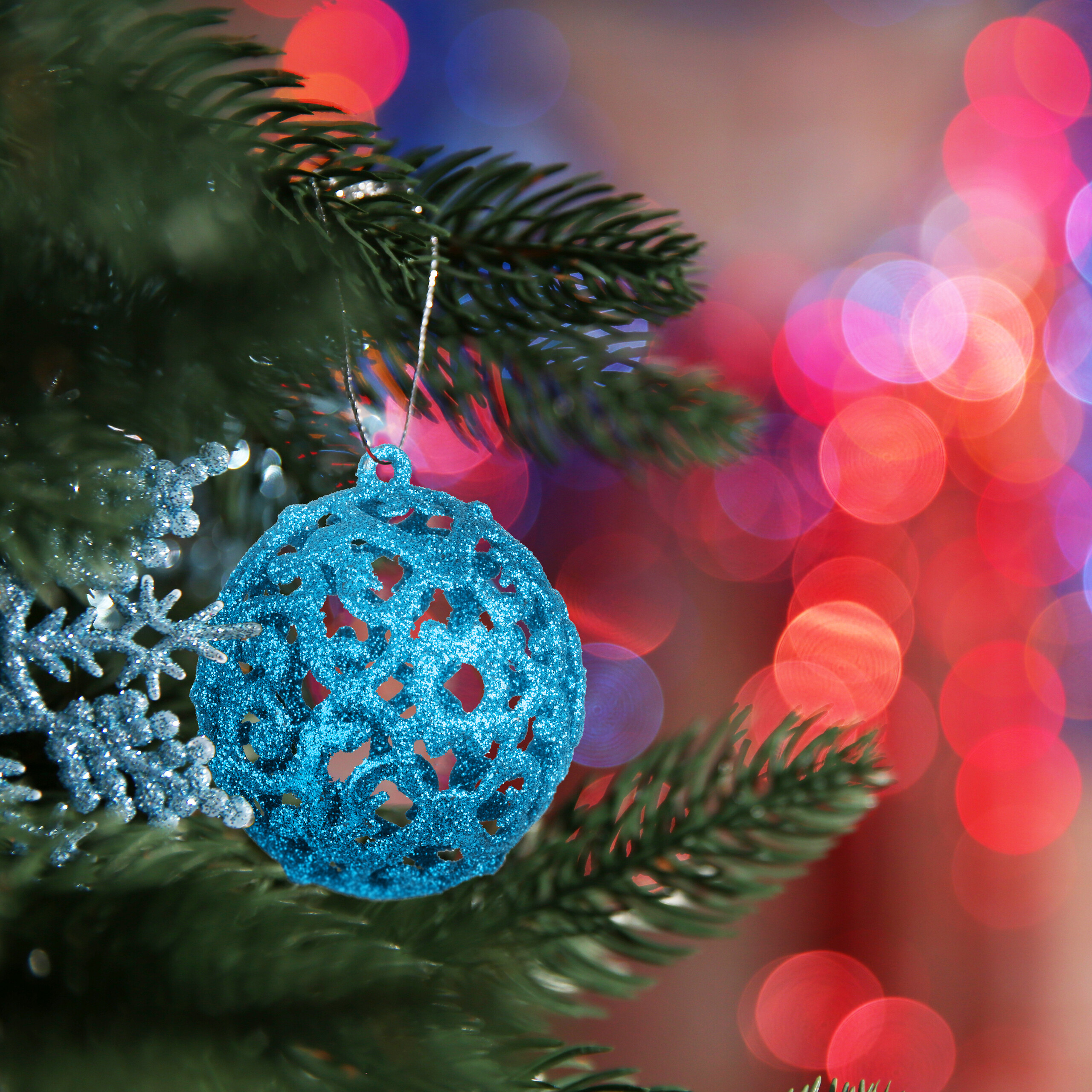 Blaue, glitzernde Weihnachtskugel hängt an einem Tannenbaum vor verschwommenem, bogenförmigem Hintergrund.
