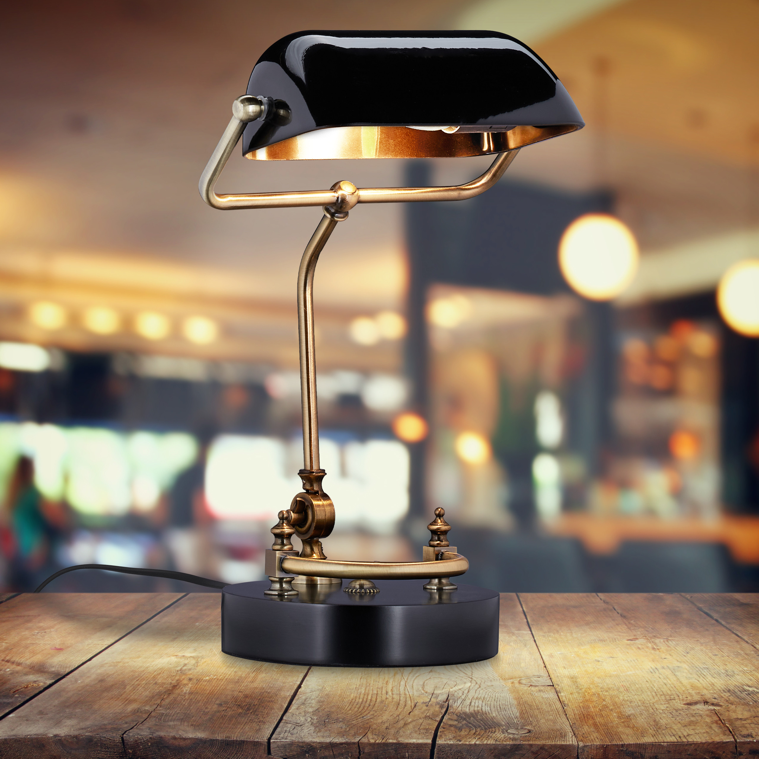 Eine schwarze und goldene Bankerlampe steht auf einem Holztisch vor verschwommenem Hintergrund.