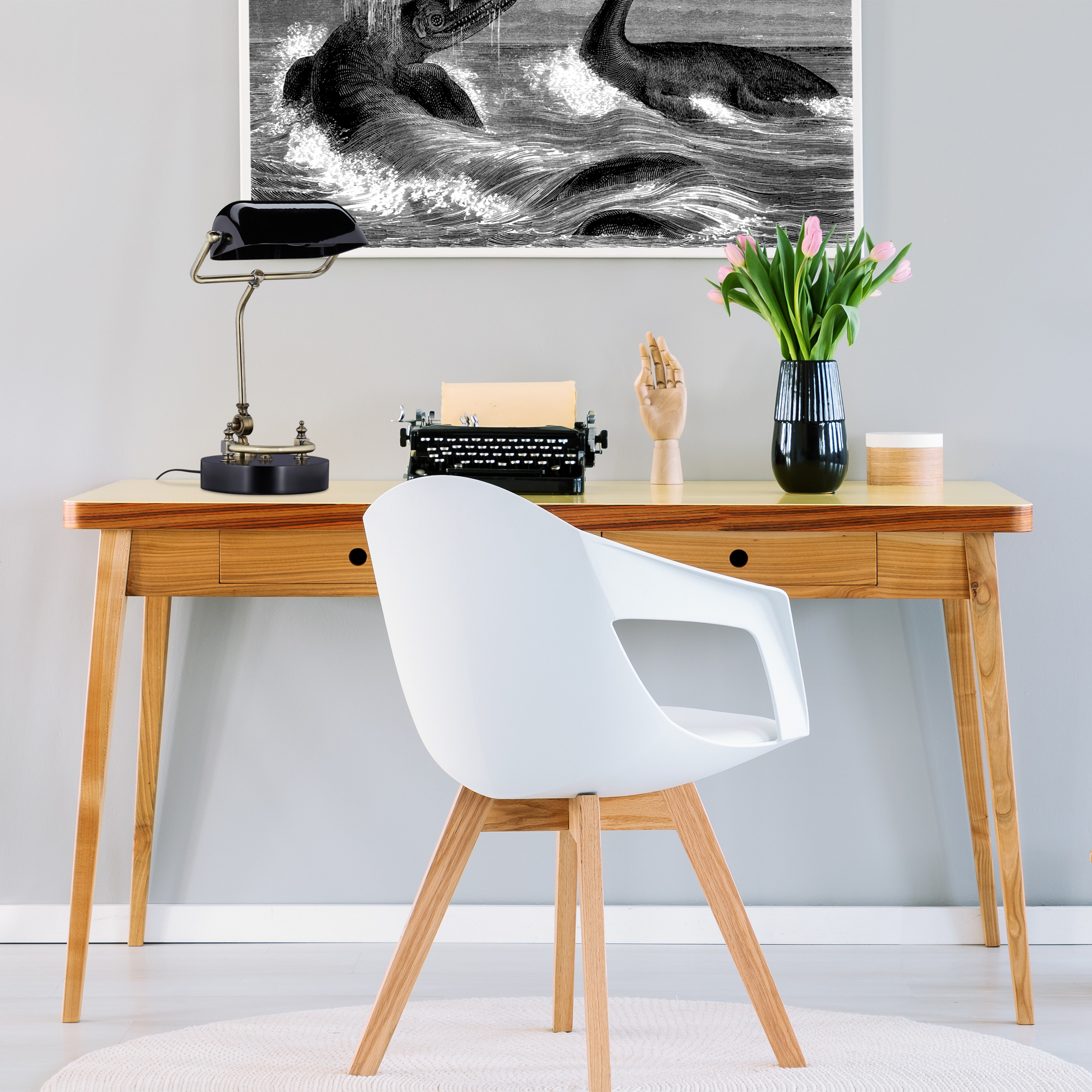 Ein Holztisch mit Lampe, Schreibmaschine und Tulpen in einer Vase. Davor ein weißer Stuhl auf weißem Teppich.