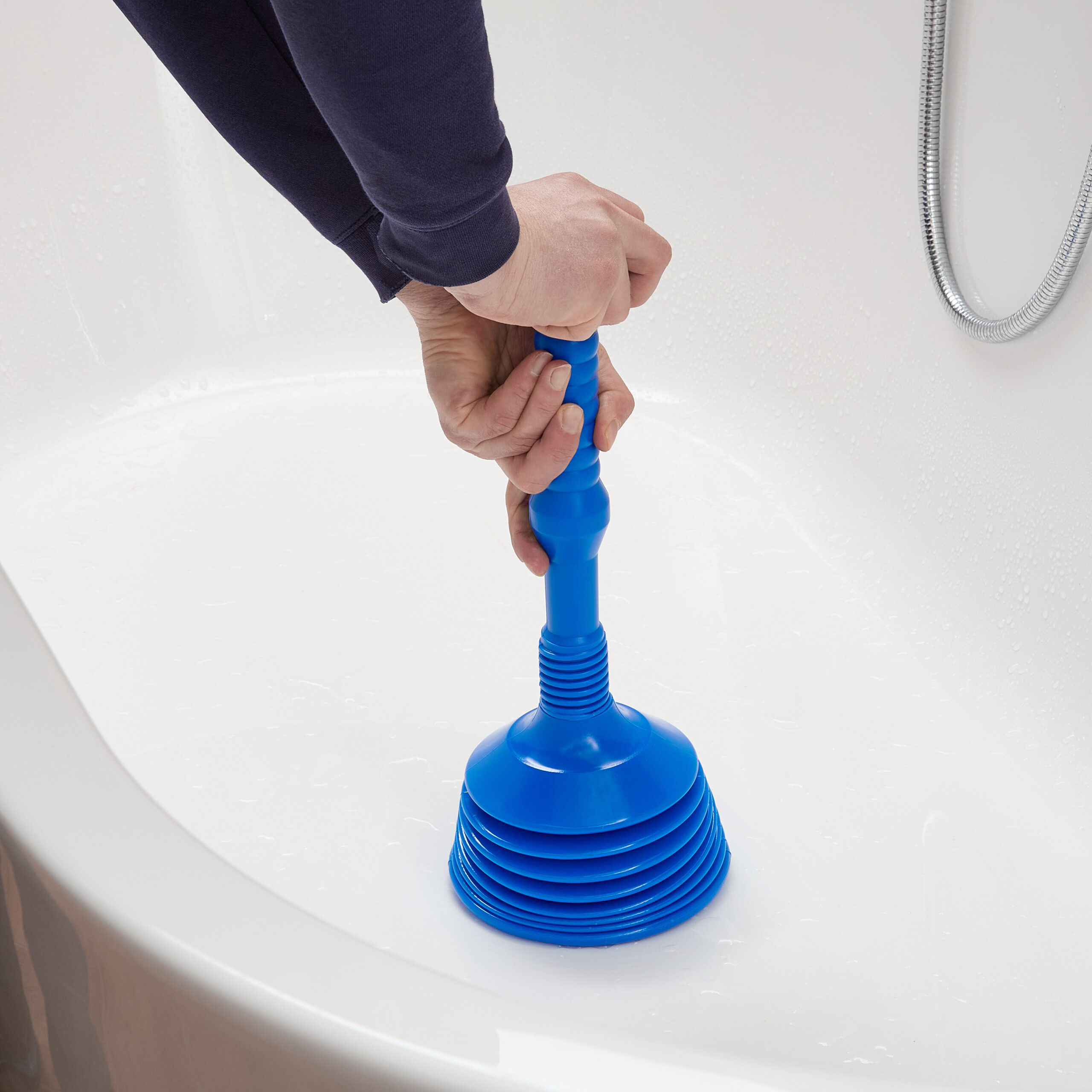 Person in dunkelblauem Pulli benutzt blauen Pümpel in weißer Badewanne.