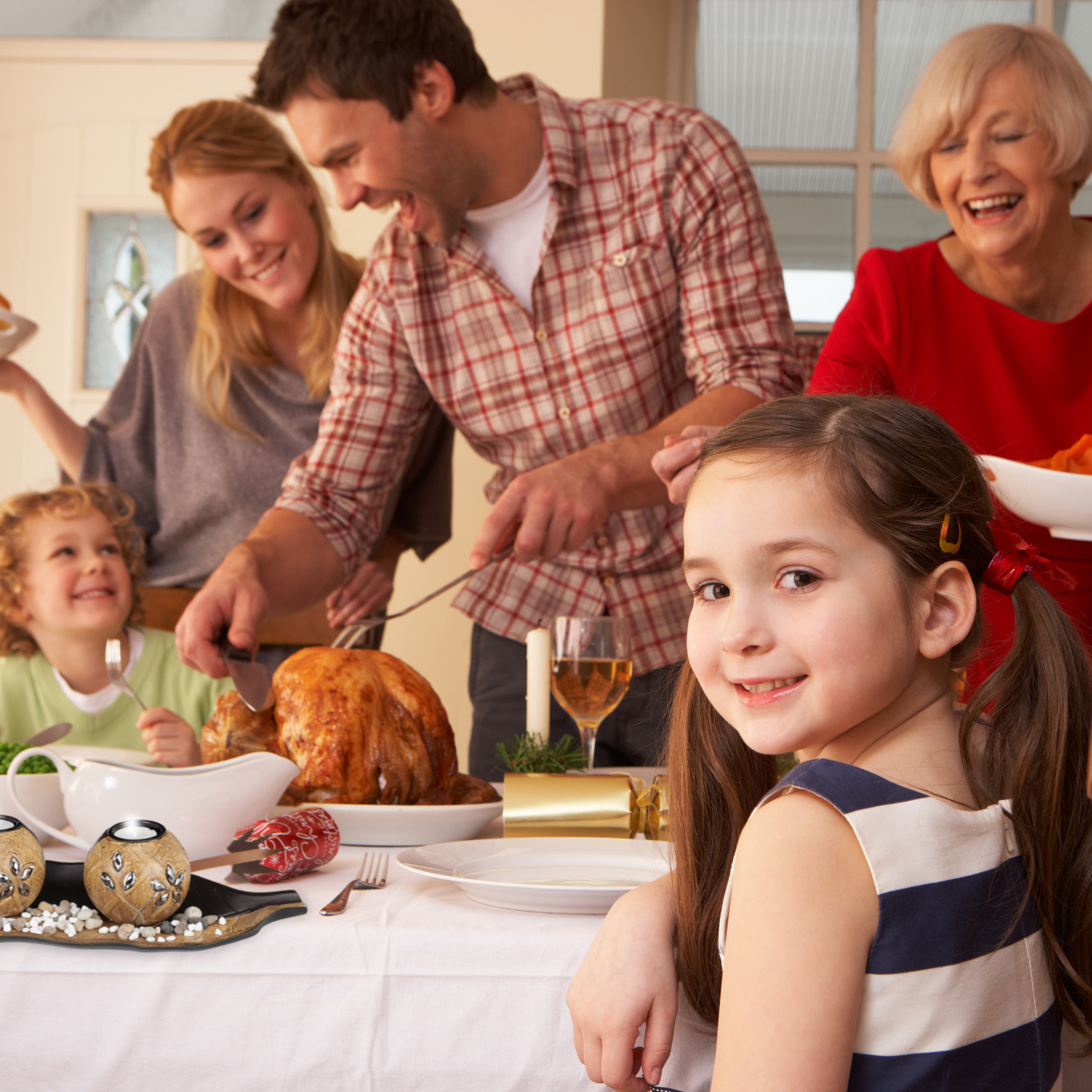 Glückliche Familie bei der Feier mit gebratenem Truthahn, ein junges Mädchen lächelt im Vordergrund.
