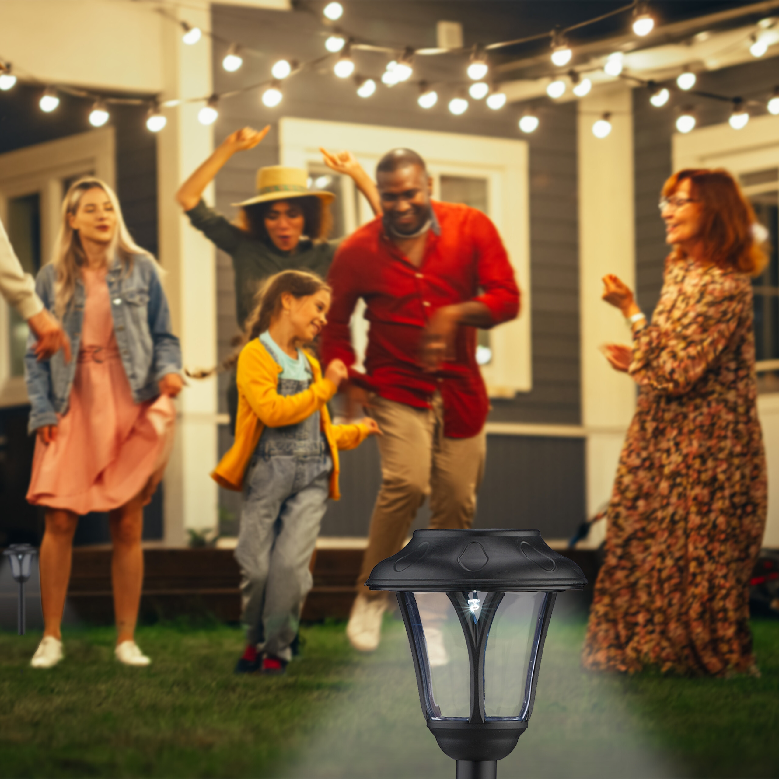 Solar-Gartenleuchte im Vordergrund, während im Hintergrund eine fröhliche Familie im Garten feiert und tanzt.