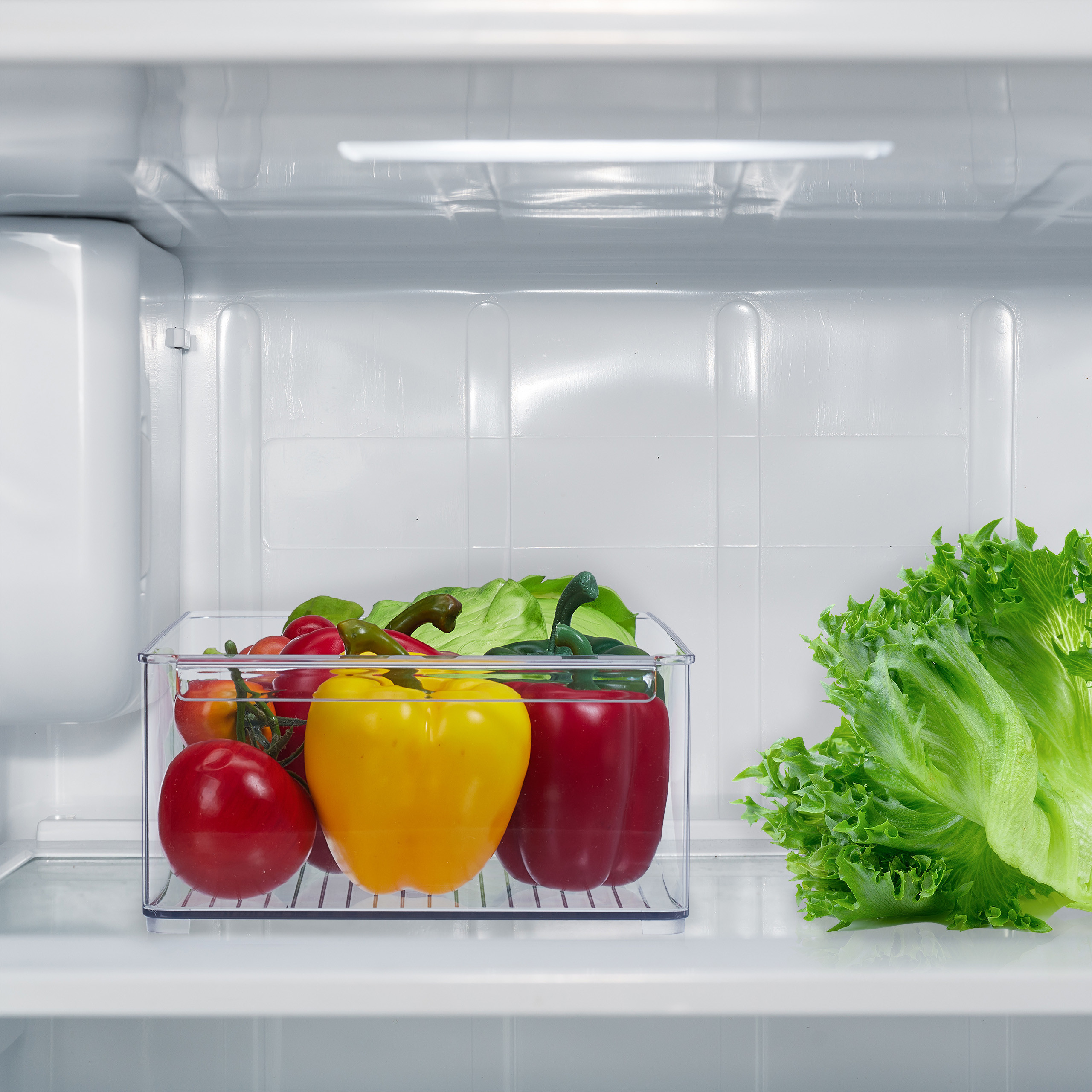 Ein offener Kühlschrank mit frischem Gemüse wie Tomaten, gelben und roten Paprika sowie grünem Salat auf dem Ablagefach.