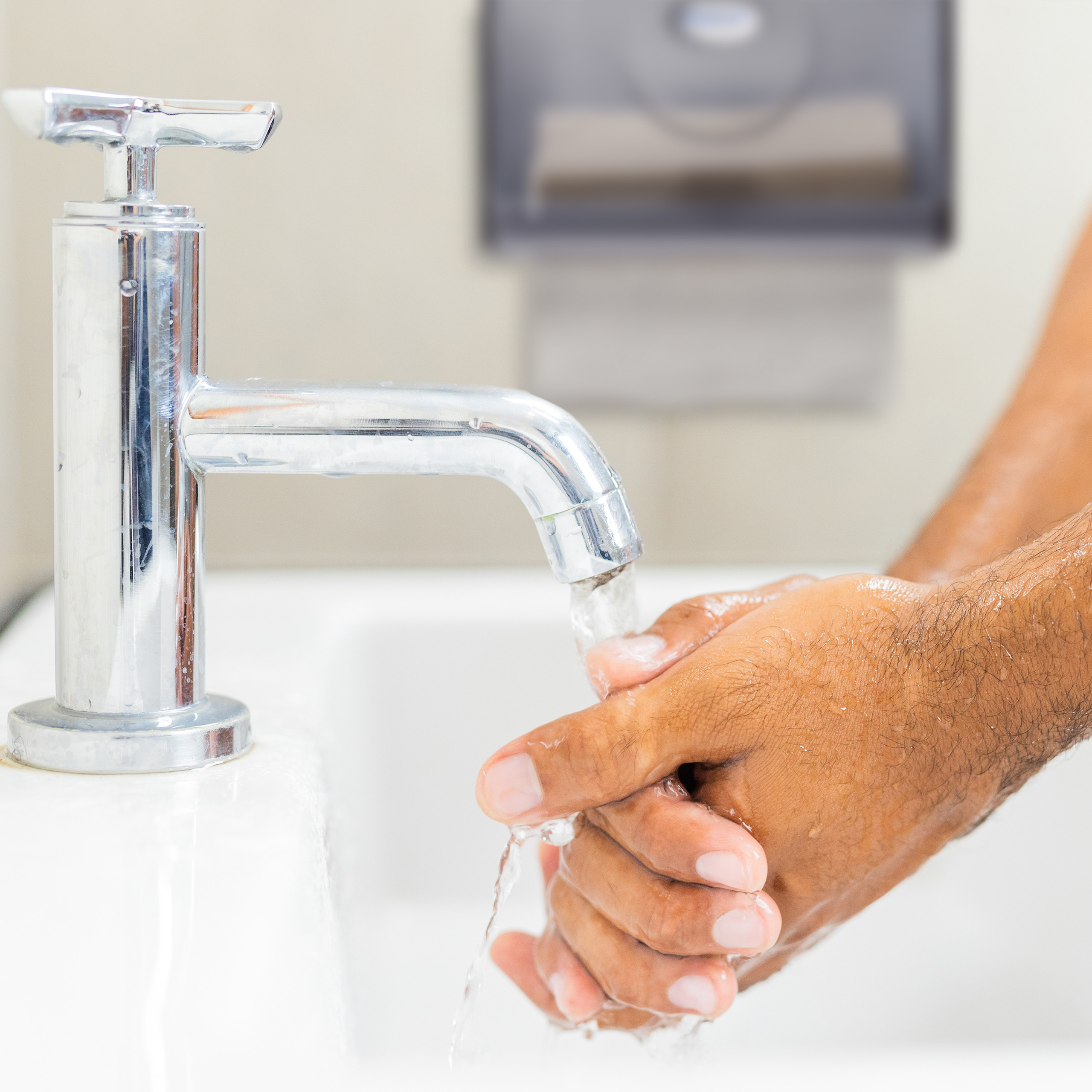 Eine Person wäscht sich die Hände unter einem verchromten Wasserhahn an einem Waschbecken.