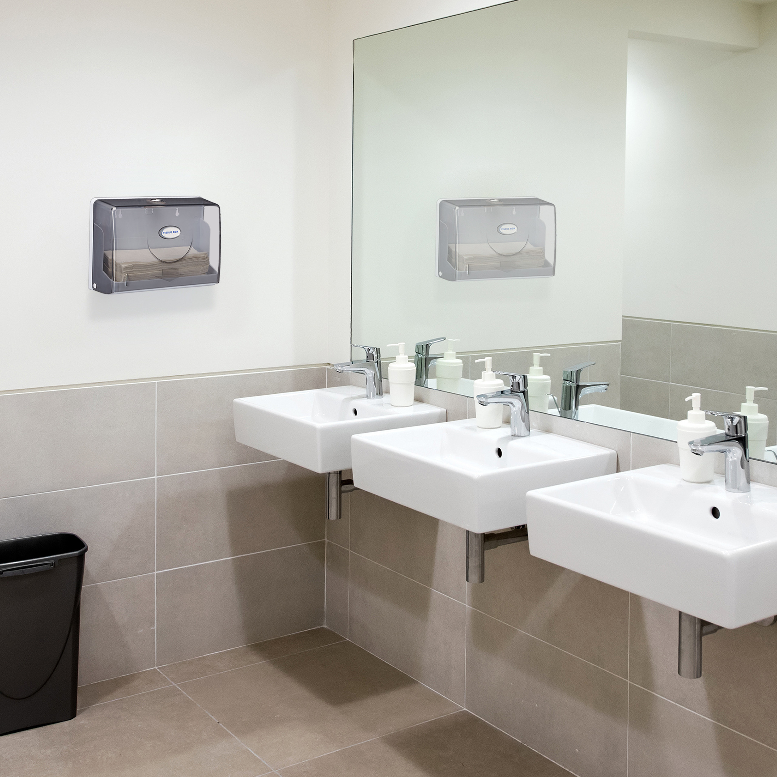 Moderne weiße Waschbecken mit Seifenspendern, einem großen Spiegel und einem Papiertuchspender an der beigen Wand.