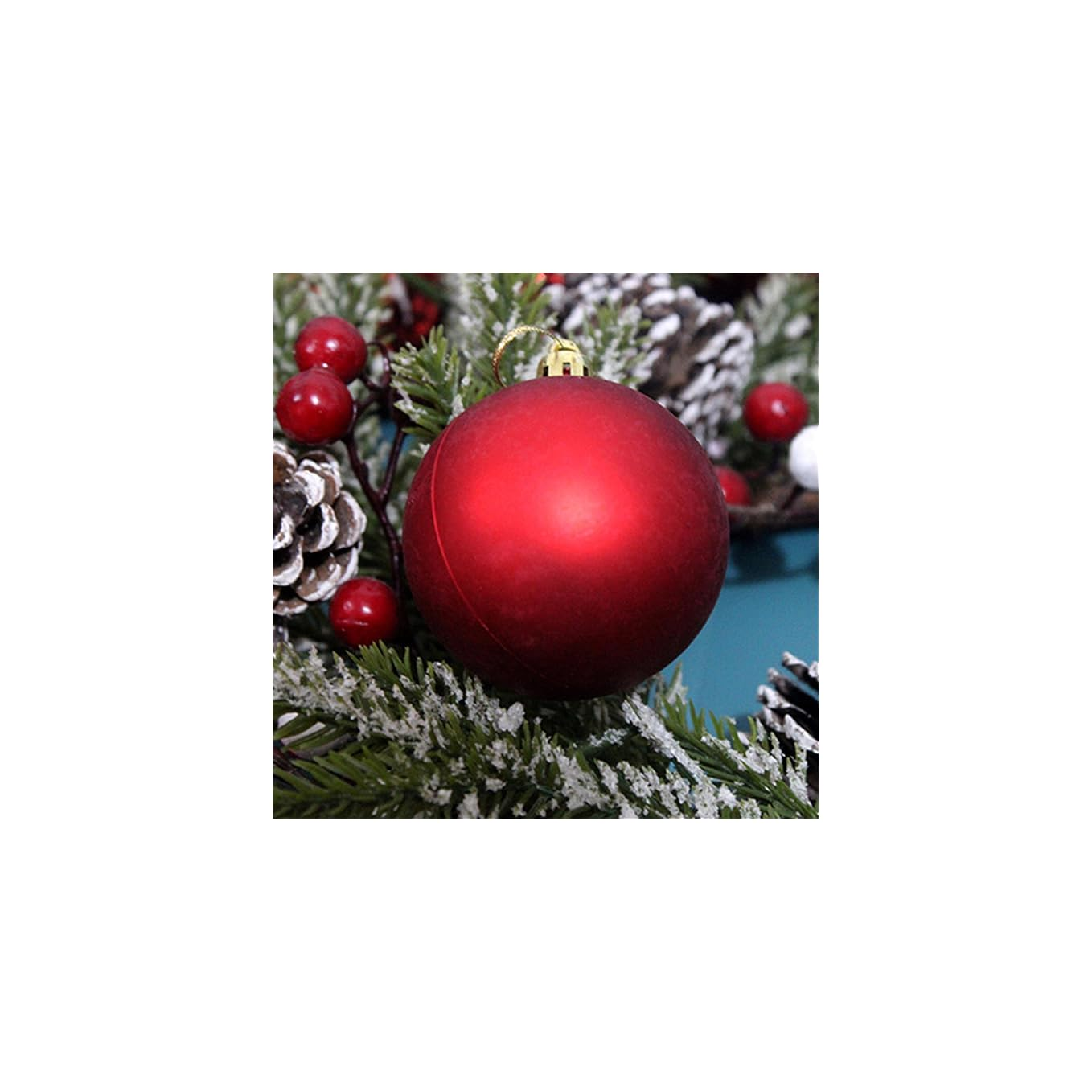 Eine matte rote Weihnachtskugel ruht auf verschneiten Tannenzweigen mit roten Beeren.