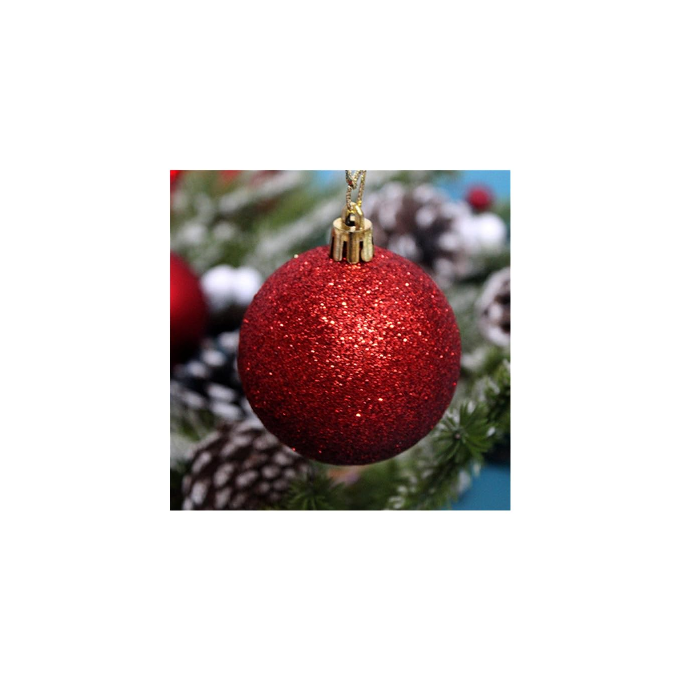 Eine glitzernde rote Weihnachtskugel hängt vor Pinienzapfen und Tannengrün.