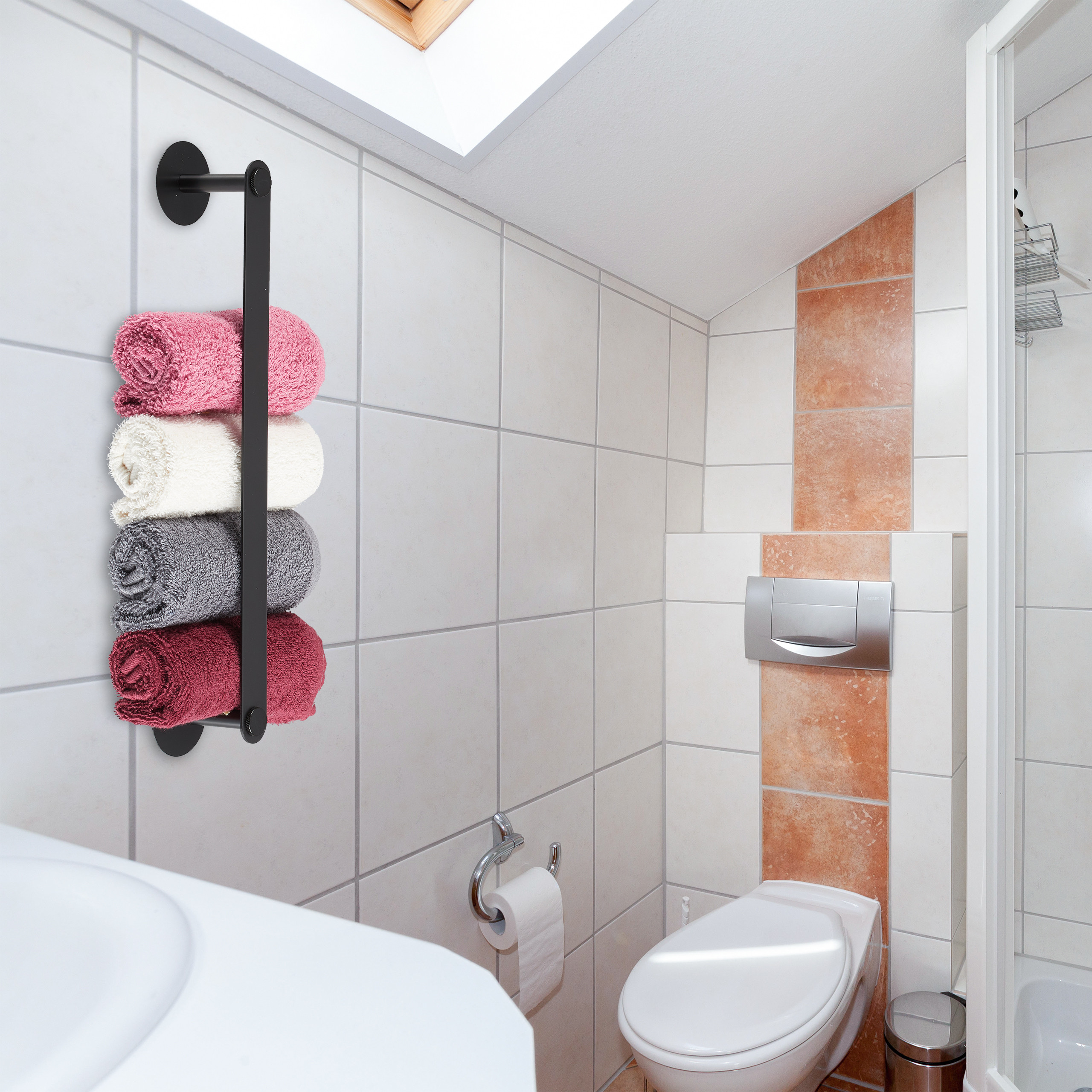 Ein schwarzer Handtuchhalter an weißen Fliesen mit rosa, weißen, grauen und roten Handtüchern; rechts Toilette.