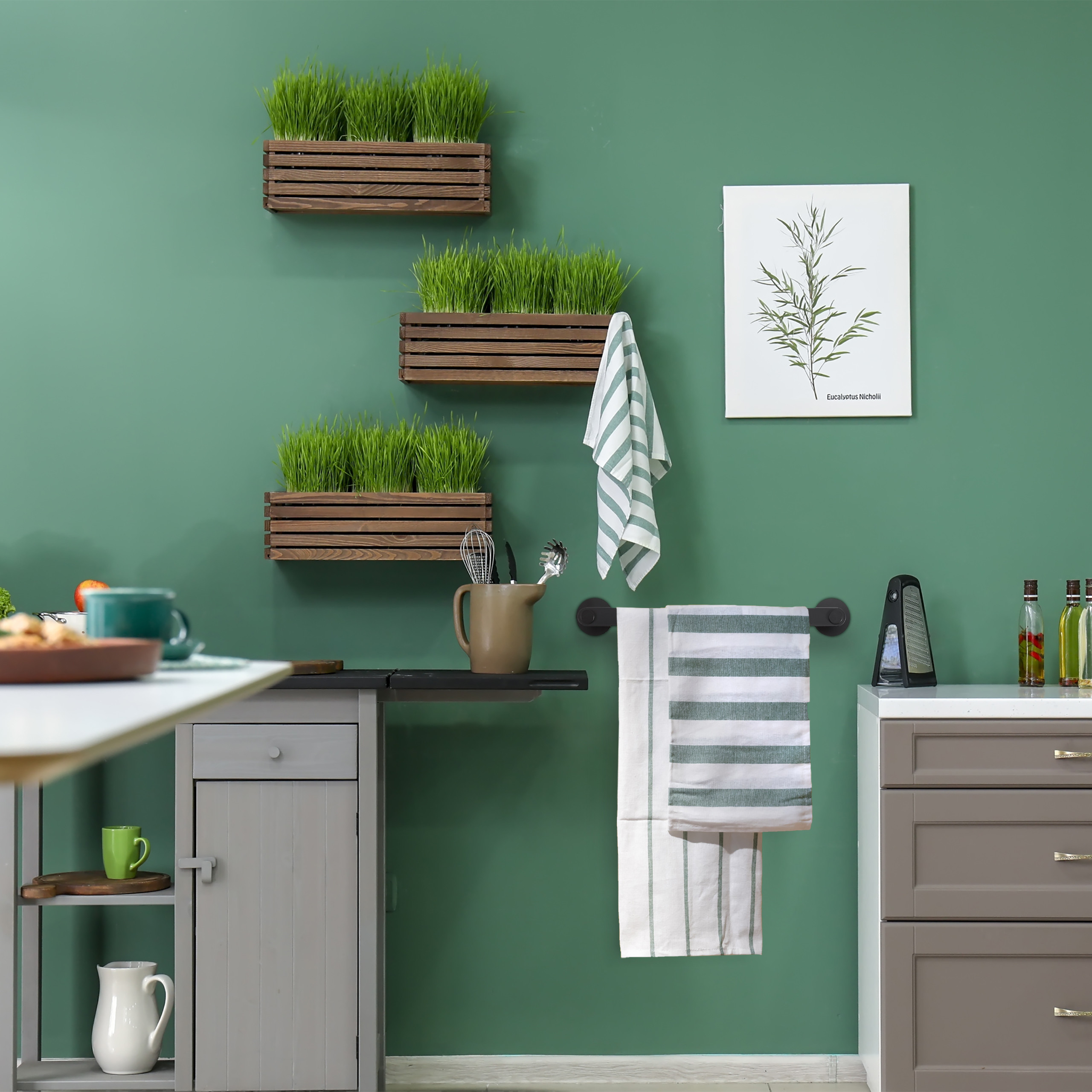 Grüne Wand mit drei Holzpflanzgefäßen, Handtüchern, Küchenschränken und einem Pflanzenbild.